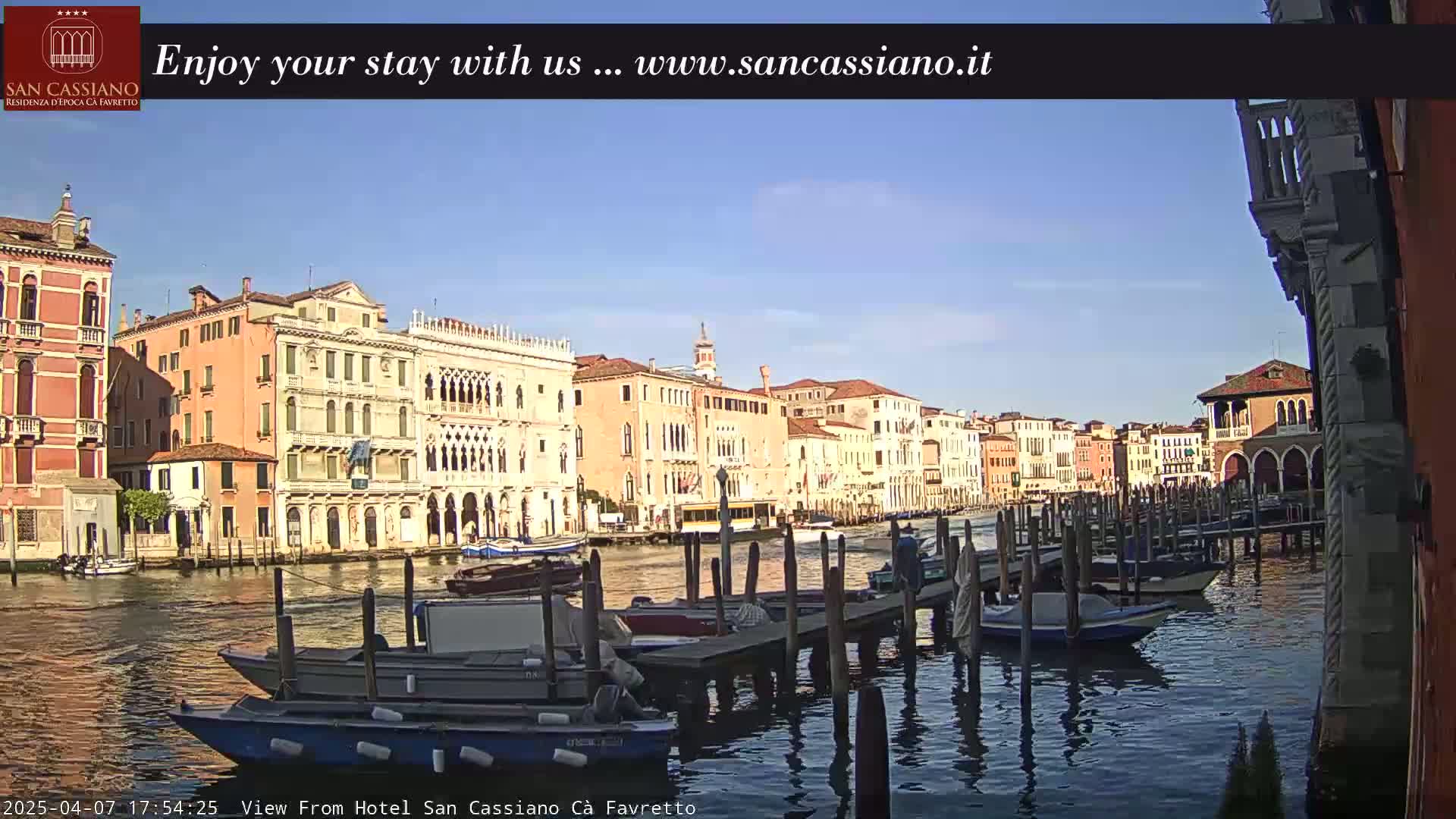 A sunny day in Venice shows a canal lined with moored boats and colorful buildings.