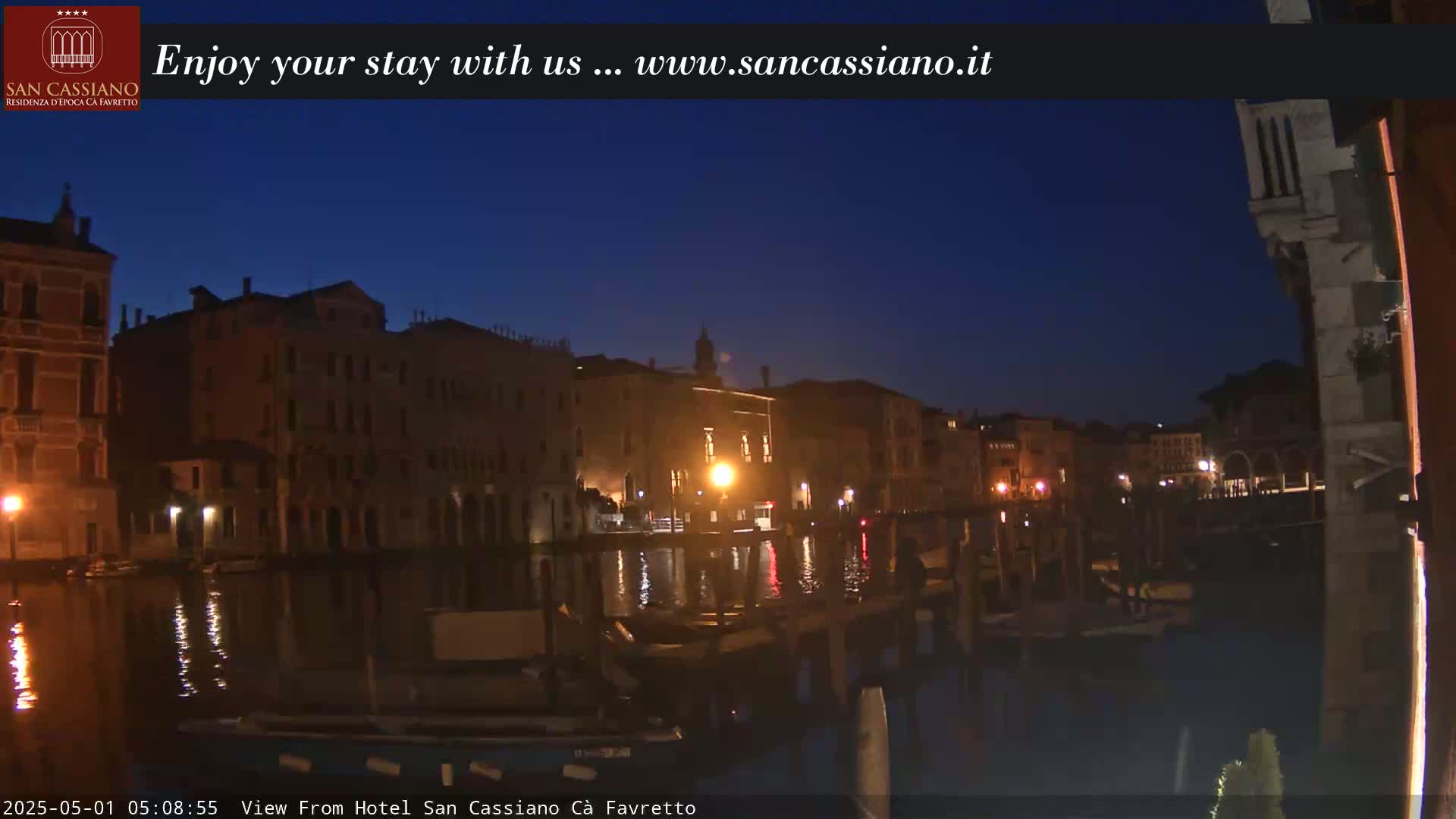 A nighttime view of a canal in Venice, Italy, with dark buildings lining the water's edge, and a few lights visible.