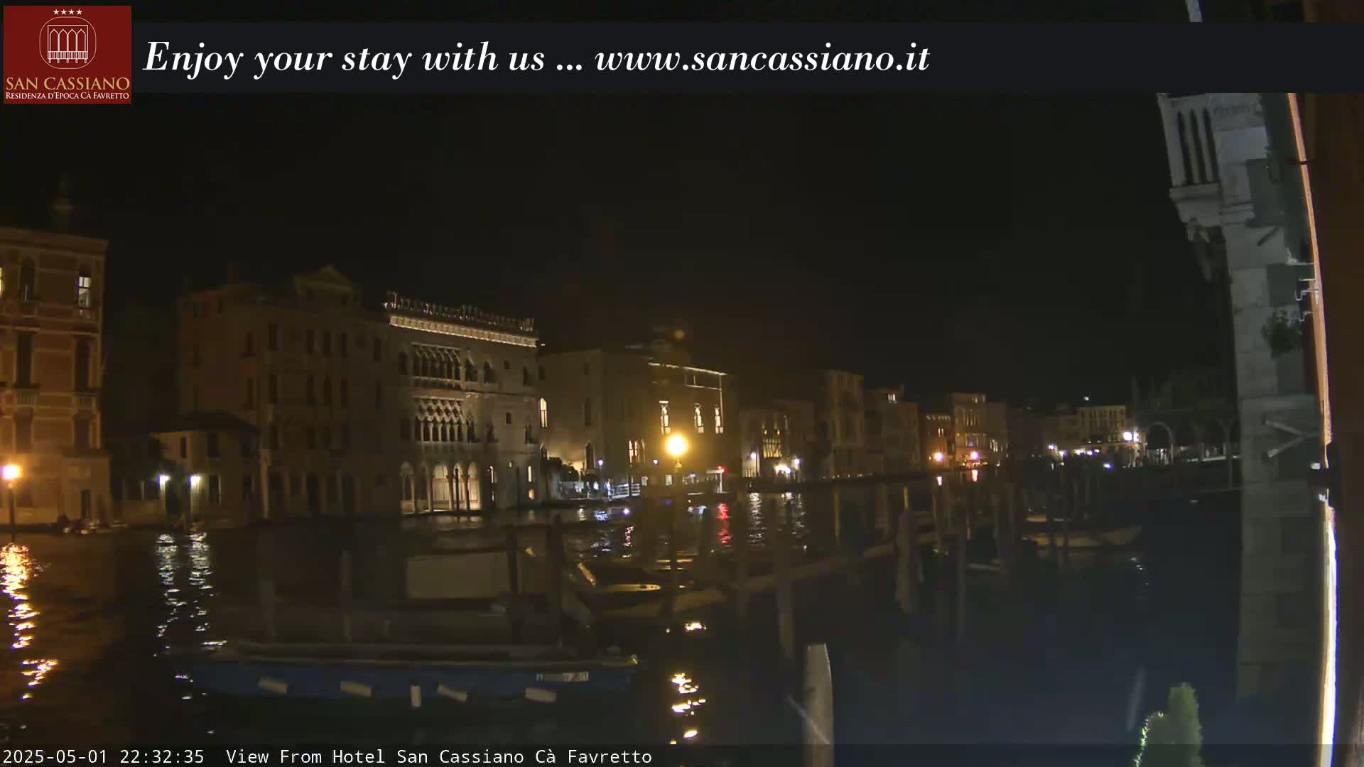 A nighttime view of a canal in Venice, showing illuminated buildings along the waterfront.