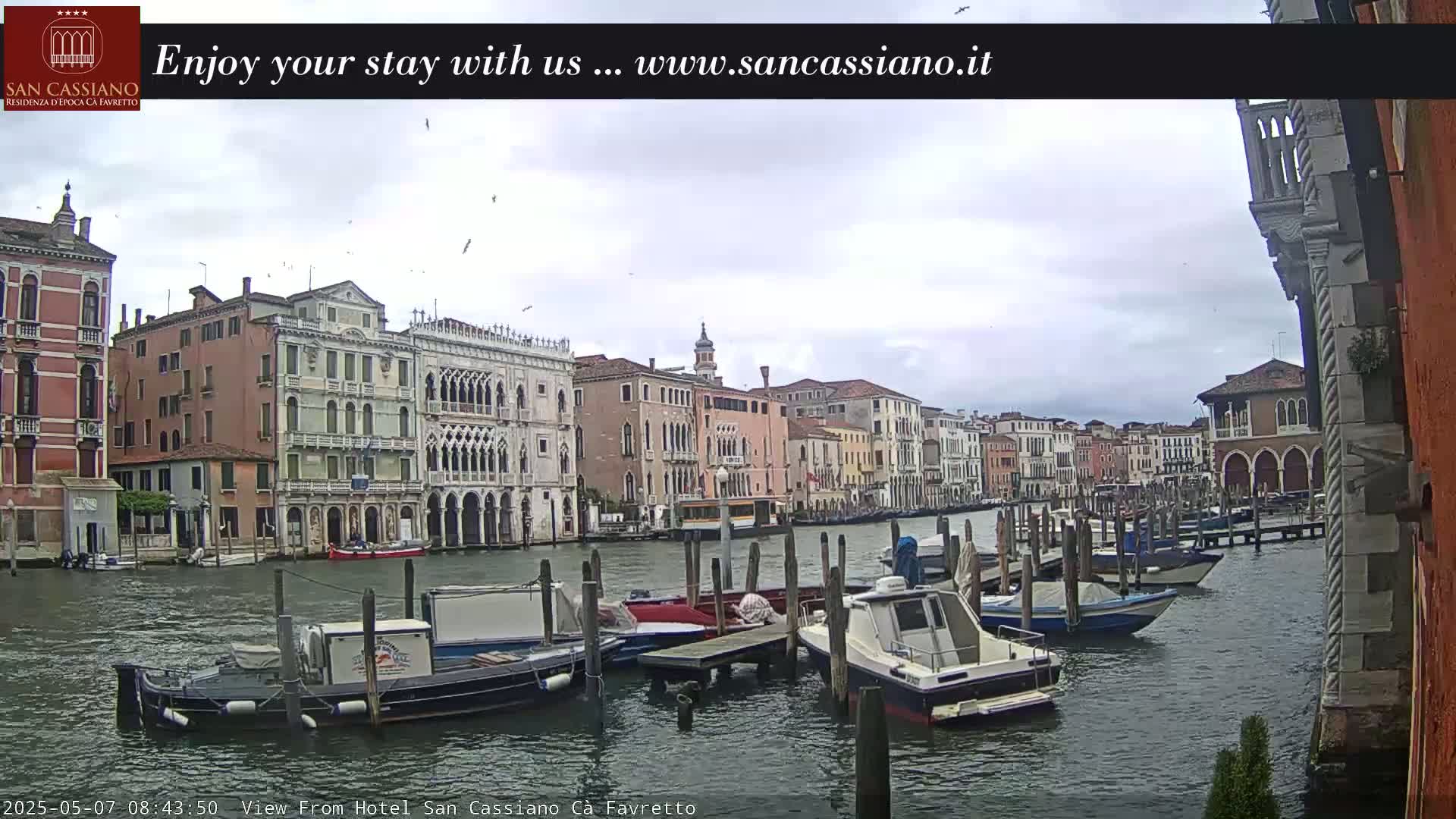 Several boats are moored along a canal in Venice, Italy, under an overcast sky.