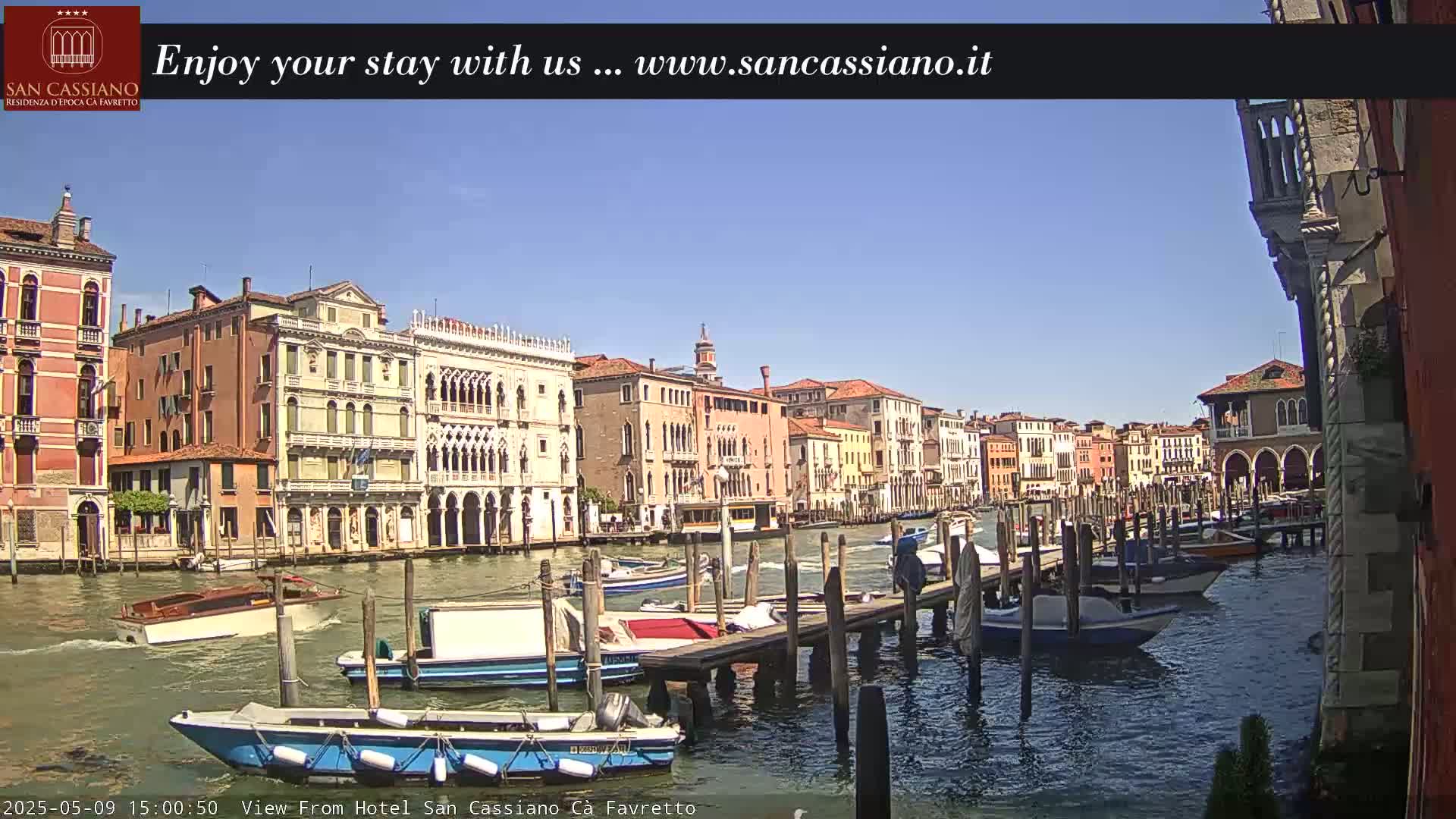 A sunny day in Venice shows a canal lined with colorful buildings and numerous boats moored at wooden docks.