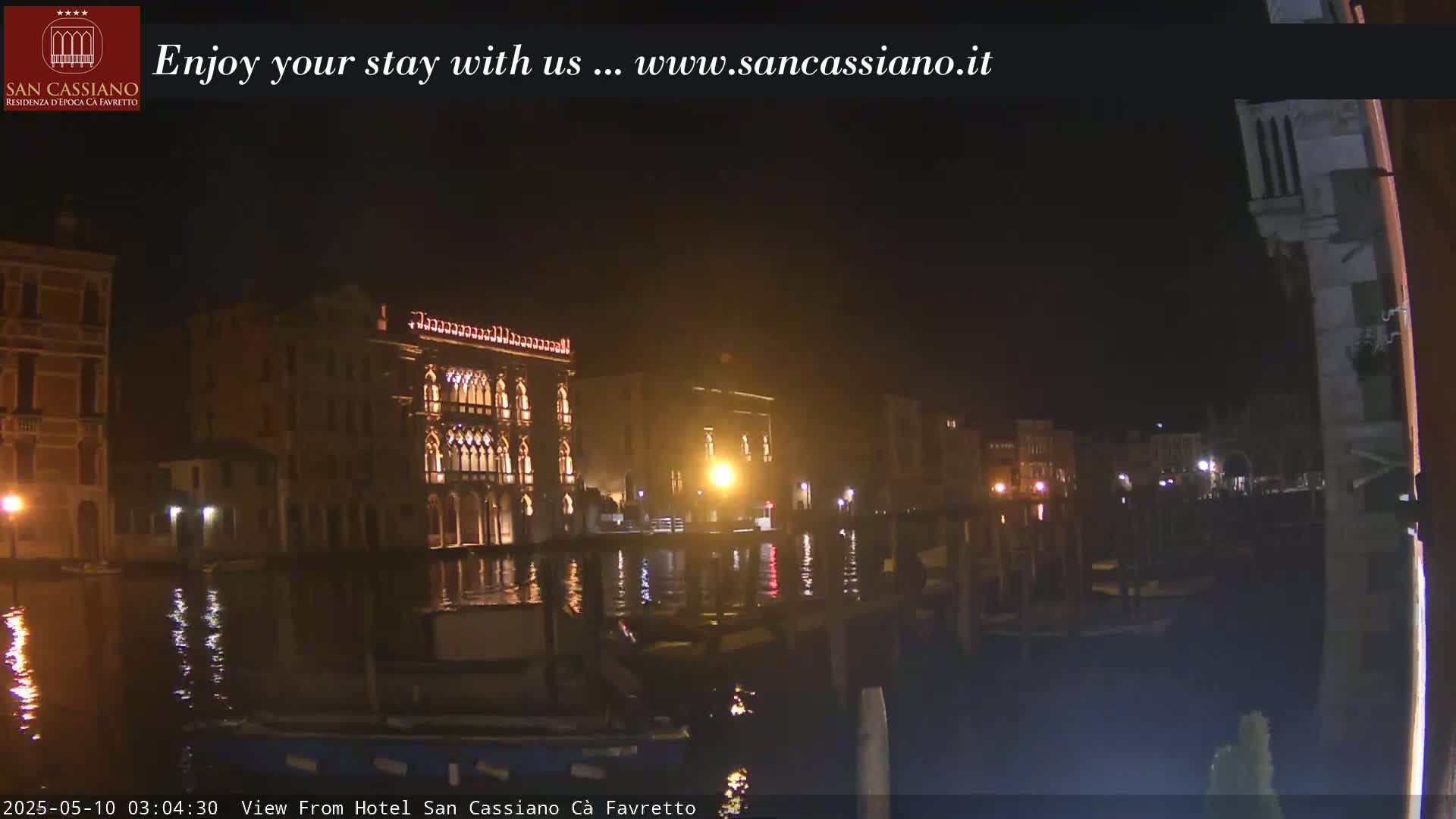 A nighttime view across a calm canal shows several illuminated buildings along its banks.