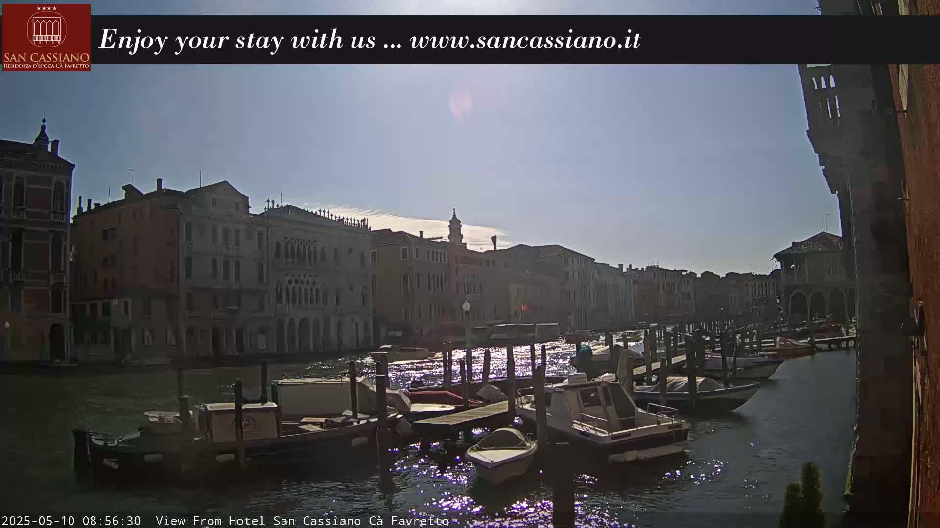 A sunny day in Venice shows a canal lined with old buildings and numerous boats moored at docks.