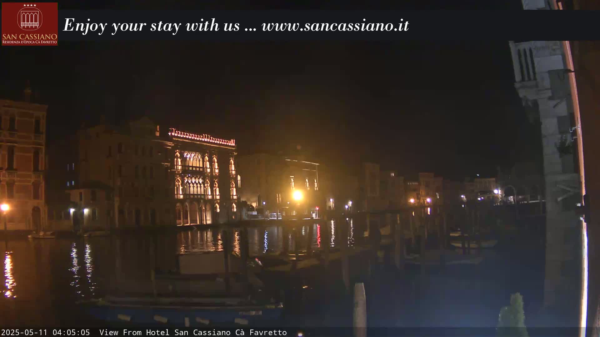 Illuminated buildings line a canal at night, their reflections shimmering on the dark water.