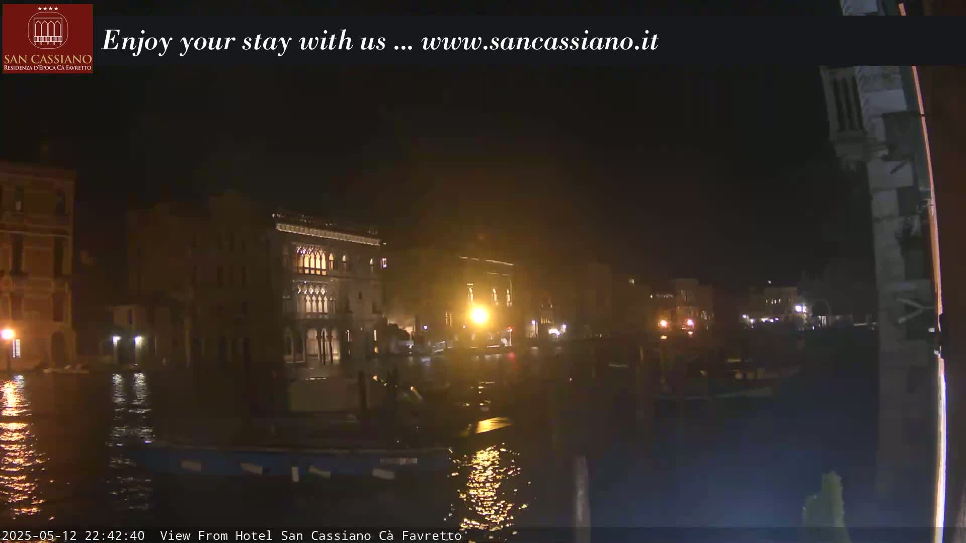 A nighttime view of dimly lit buildings across a canal, with boats moored along the waterfront.