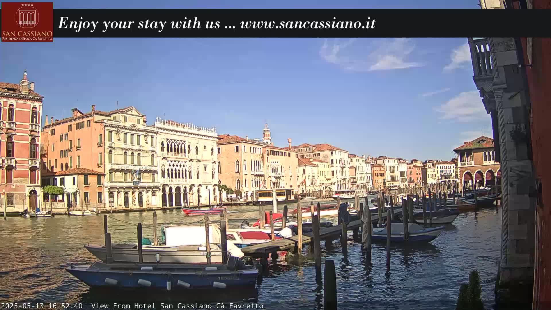 A sunny day in Venice shows colorful buildings lining a canal, where several boats are moored at docks.