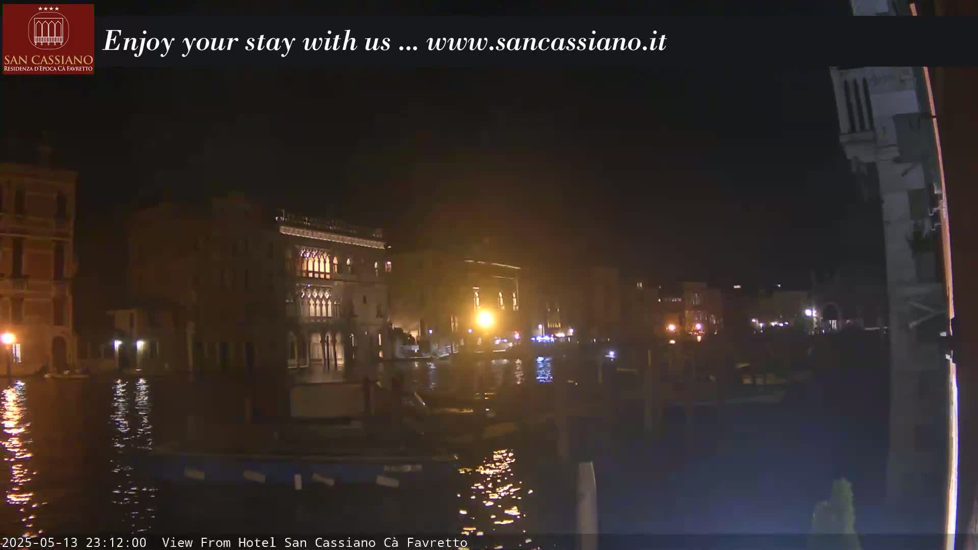 A nighttime view across a calm canal shows several illuminated buildings along its edge.