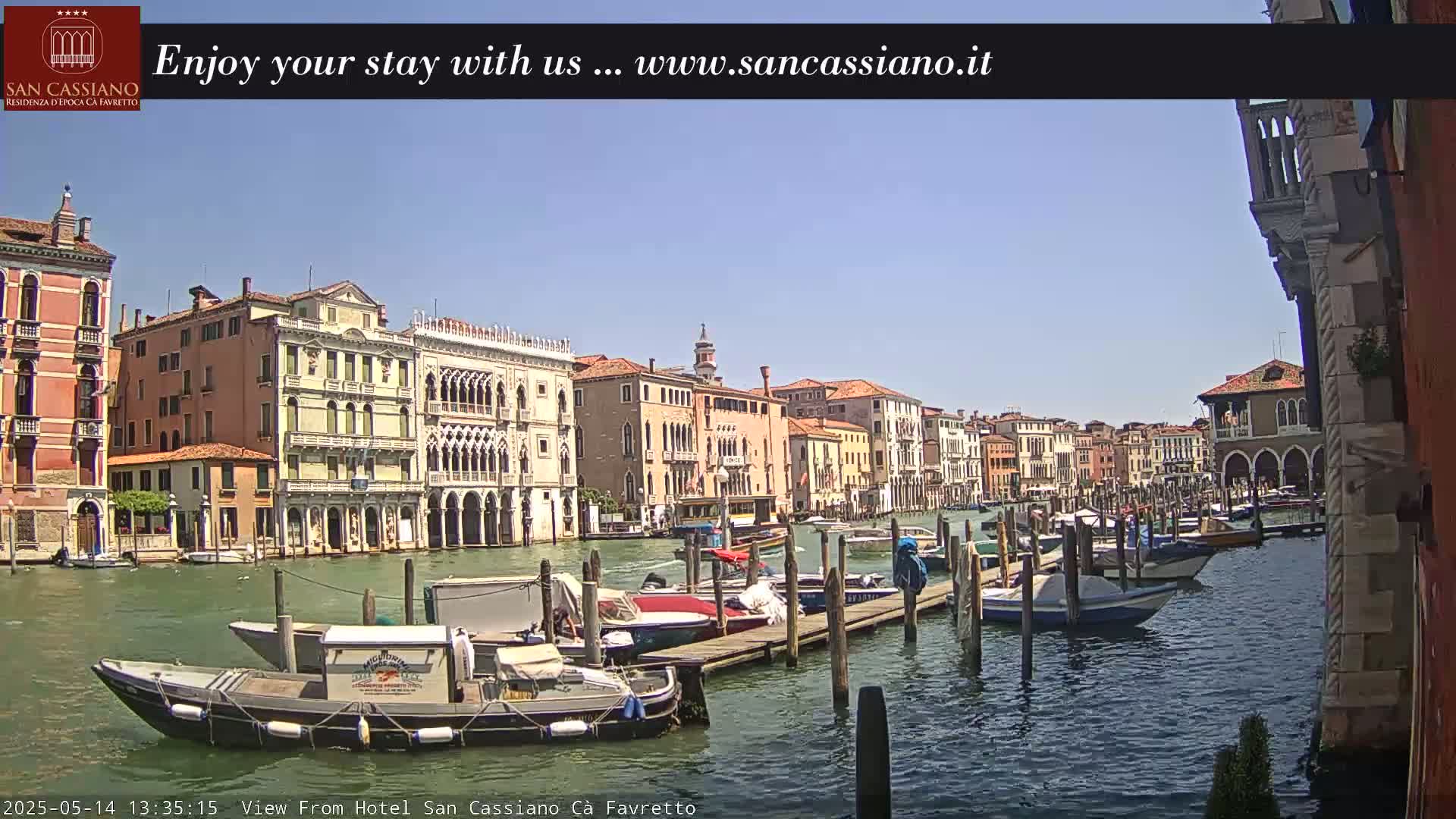 A sunny day in Venice shows colorful buildings lining a canal, where numerous boats are moored at a dock.