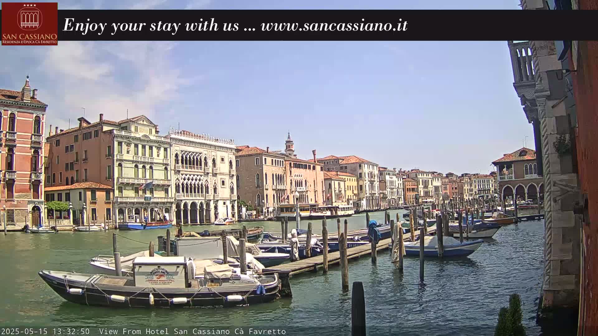 Under a clear blue sky, numerous boats are moored along a canal lined with Venetian buildings.