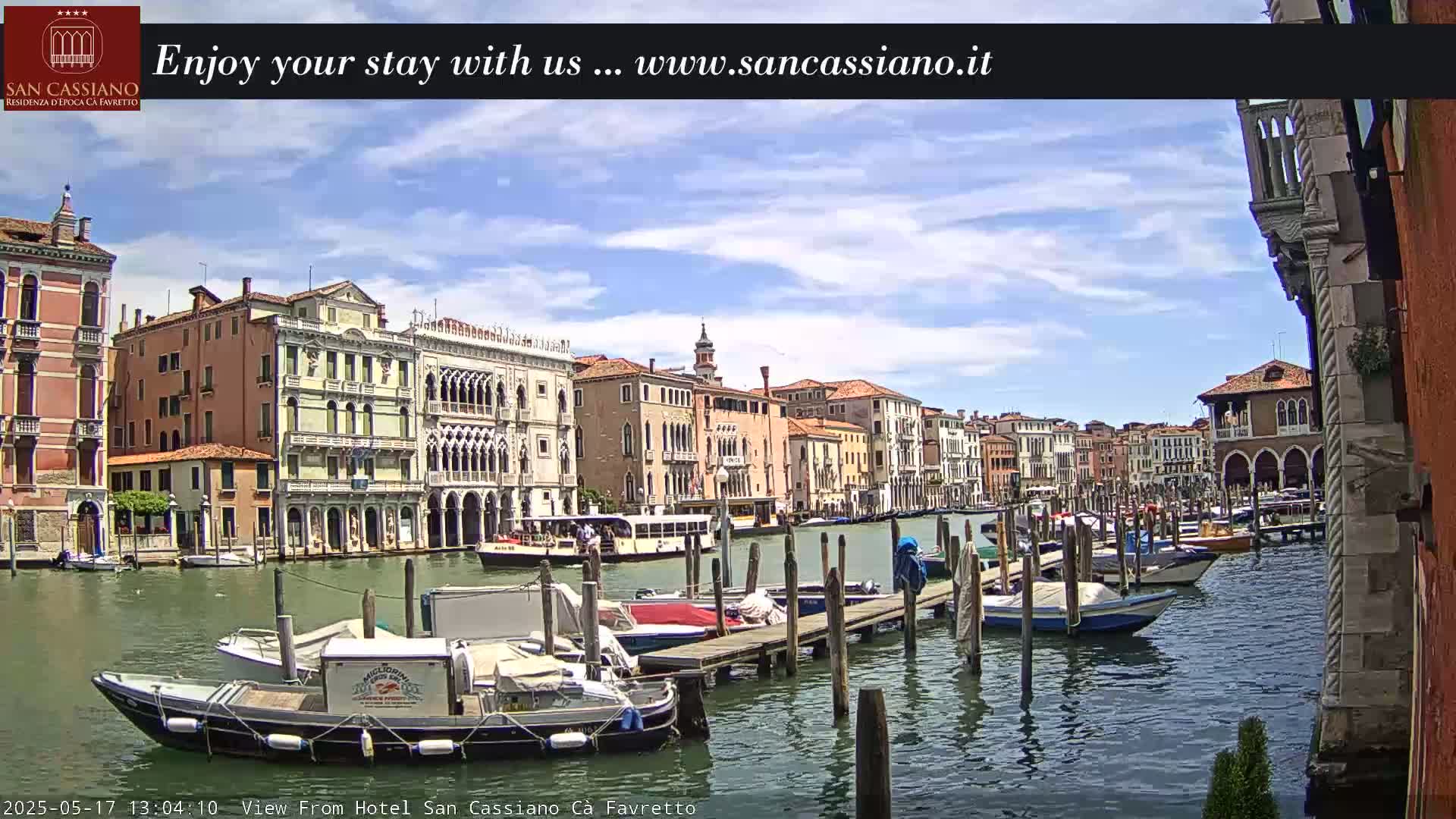 A sunny day in Venice shows a canal lined with colorful buildings and numerous boats docked at a pier.