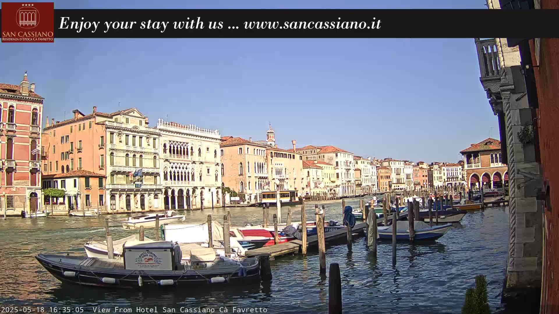 A sunny day in Venice shows a canal lined with colorful buildings and numerous boats moored at docks.