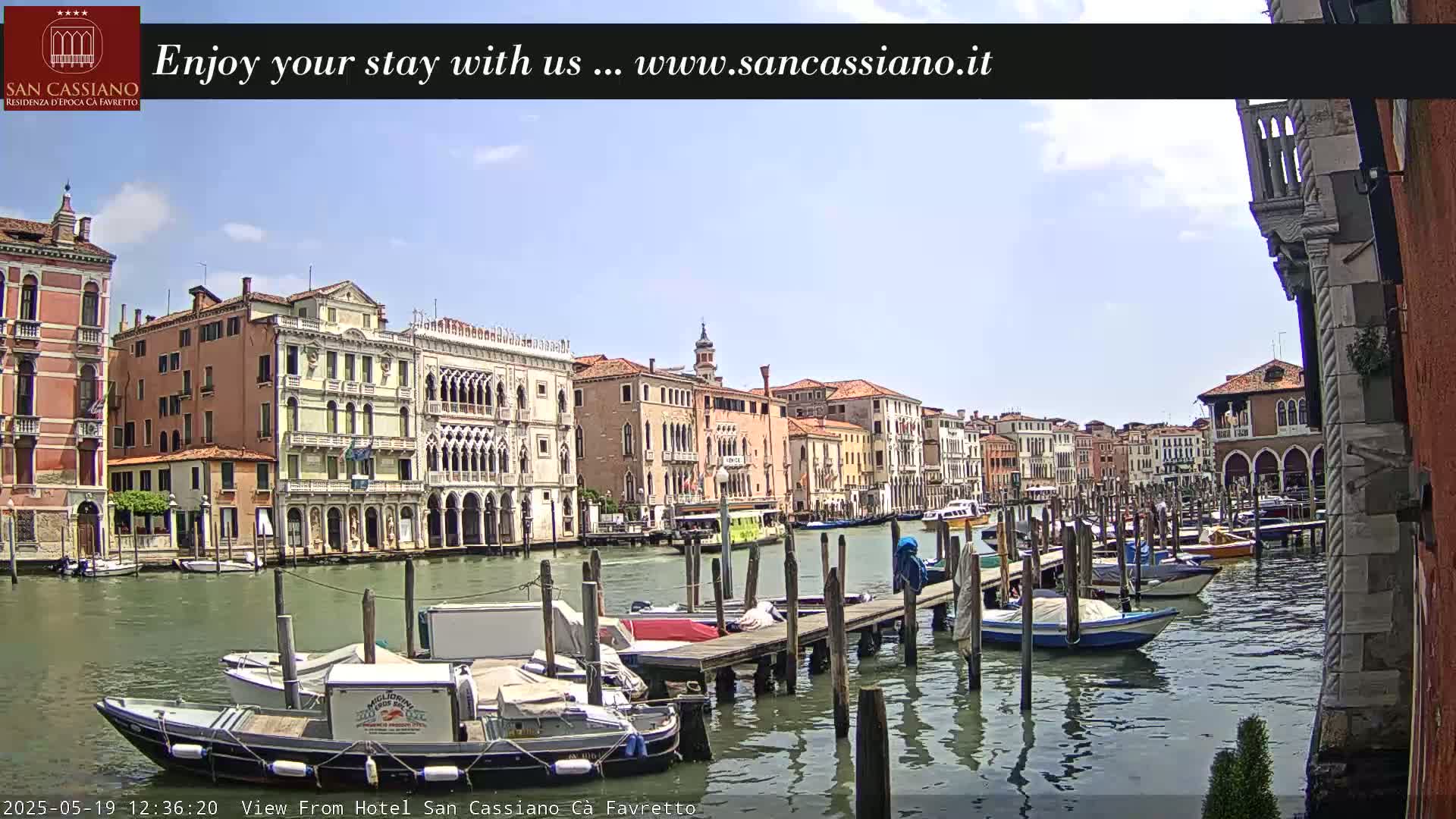 A sunny day in Venice shows a canal lined with colorful buildings and numerous boats moored at wooden docks.