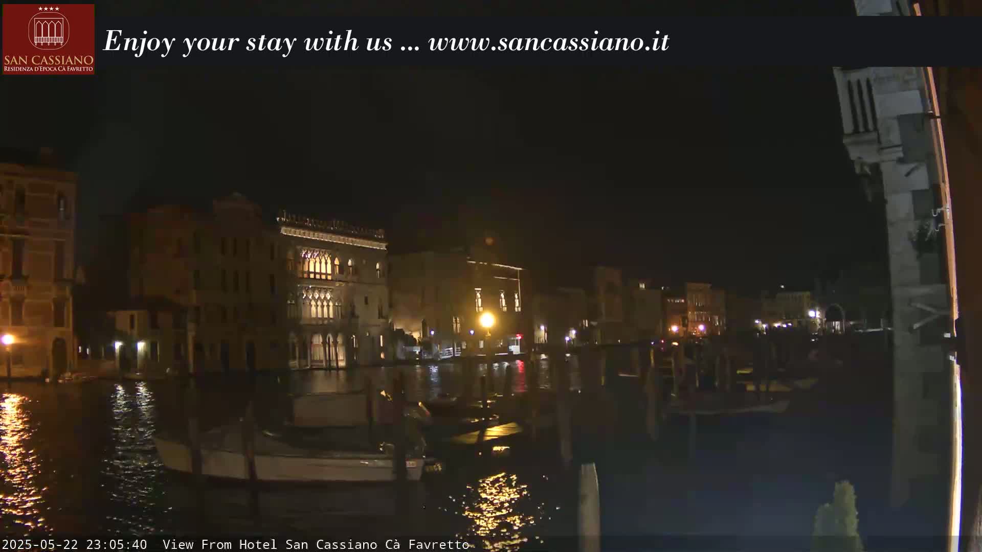 At night, several buildings are illuminated along a dark canal where small boats are moored.