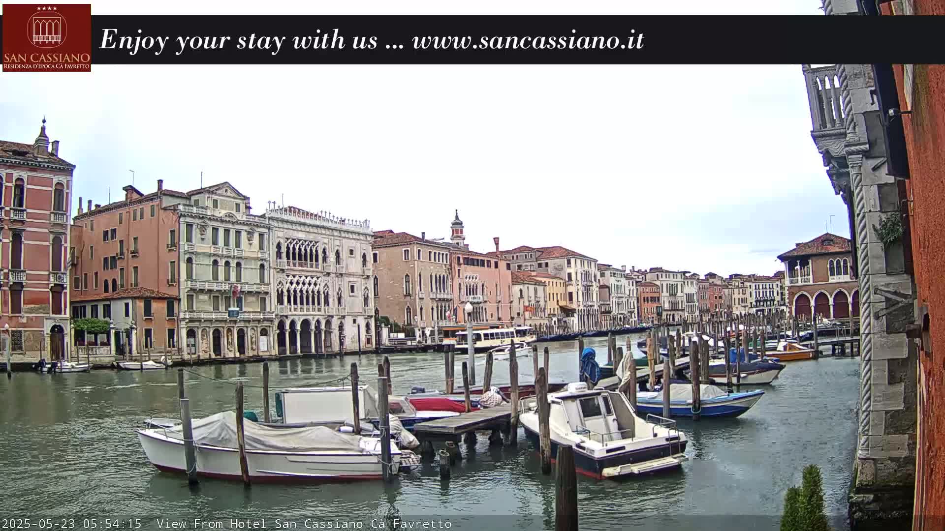 A canal in Venice, Italy, with numerous boats docked along its sides and several buildings lining the waterway under an overcast sky.