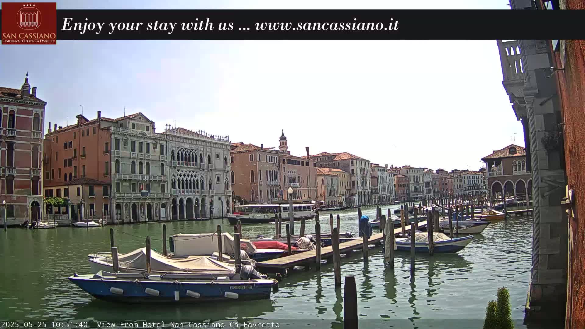 A canal in Venice, Italy, with several moored boats and buildings lining the waterway under a mostly clear sky.