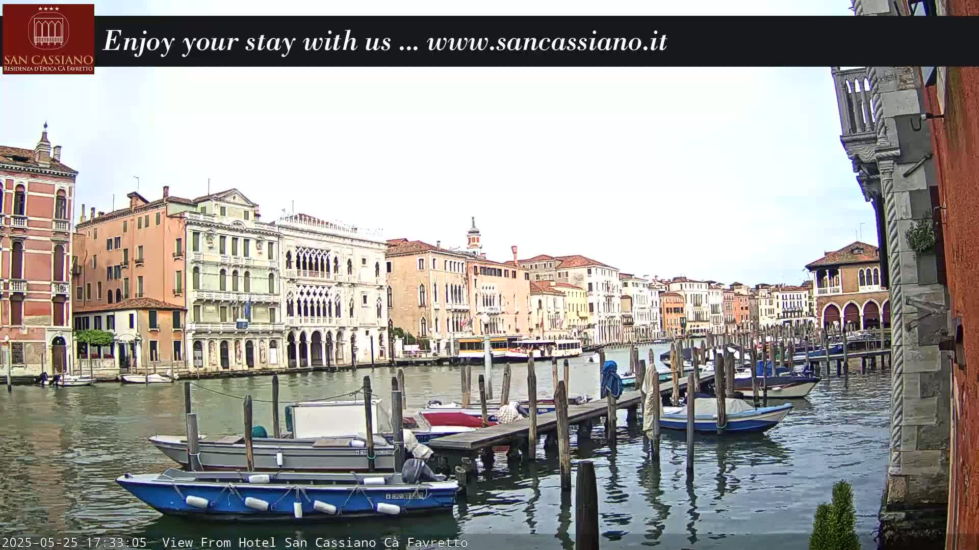A canal in Venice, Italy, with numerous boats moored at wooden docks, under an overcast sky.