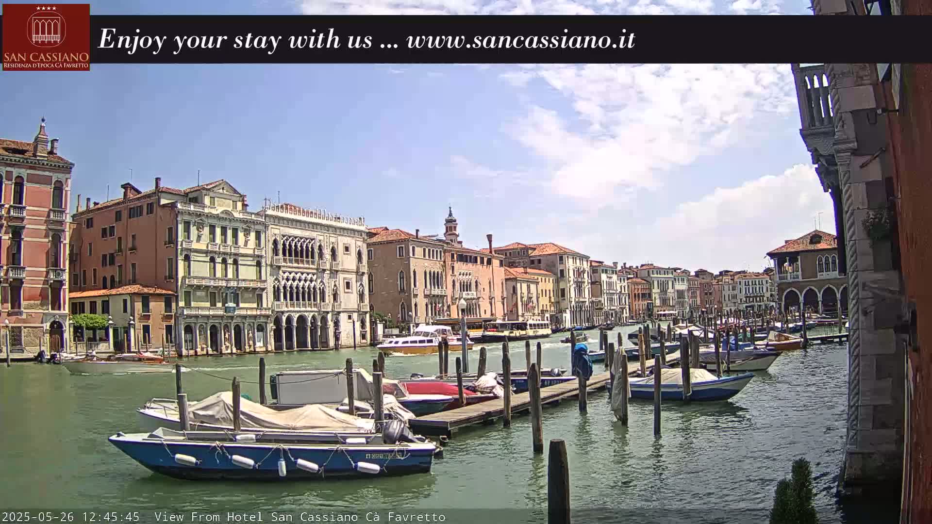 A sunny day in Venice shows a canal lined with colorful buildings and numerous boats moored at wooden docks.