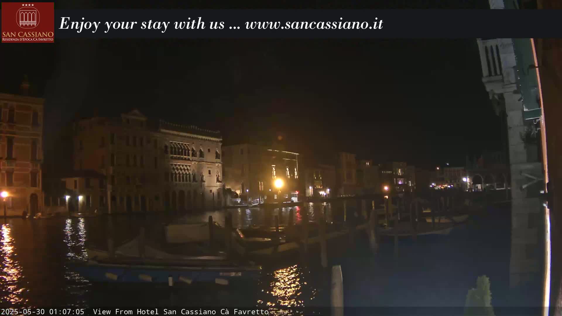 A nighttime view of a canal in Venice, Italy, shows several buildings along the waterway with boats moored nearby.