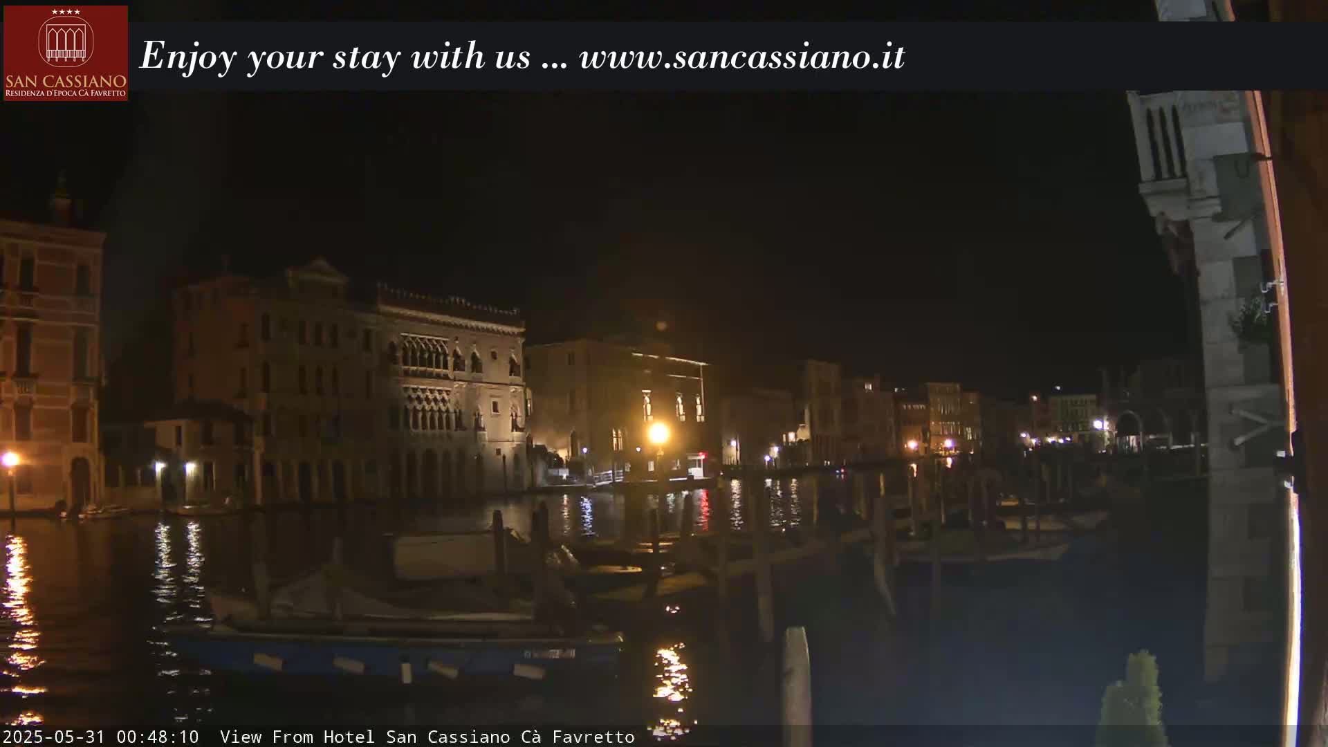 A nighttime view of a canal in Venice, Italy, with several buildings lit along the waterway.