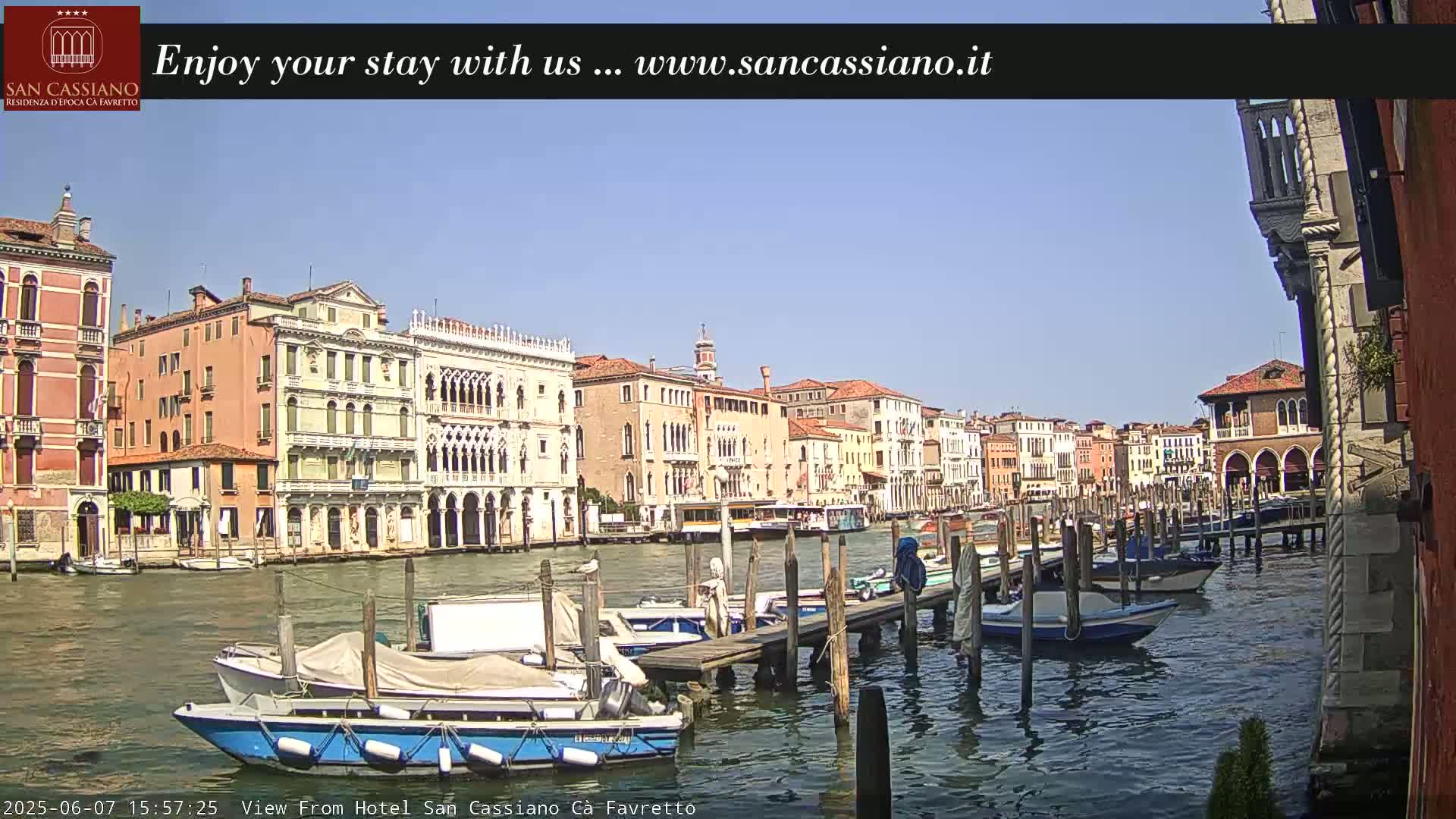 A sunny day in Venice shows several boats docked along a canal, with colorful buildings lining the waterway.