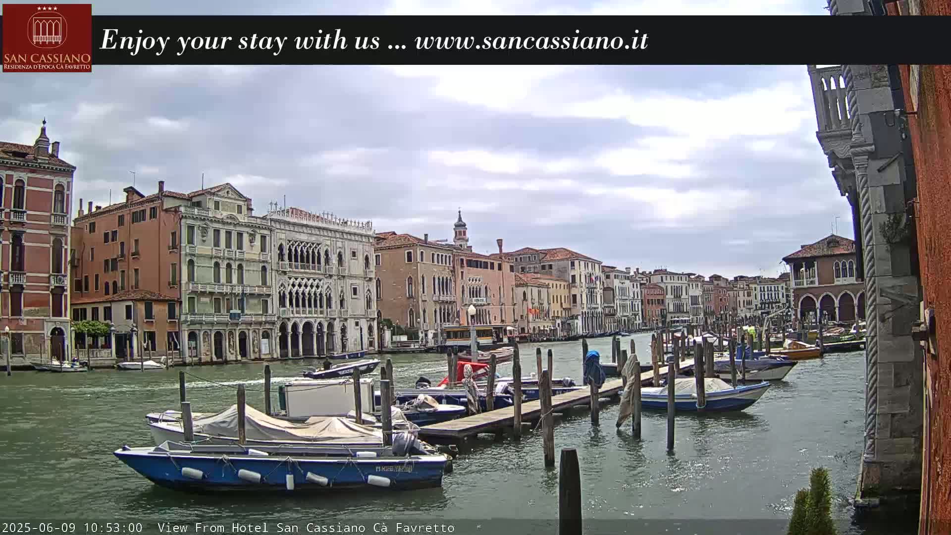 A canal in Venice, under a cloudy sky, is lined with colorful buildings and numerous boats moored at a dock.