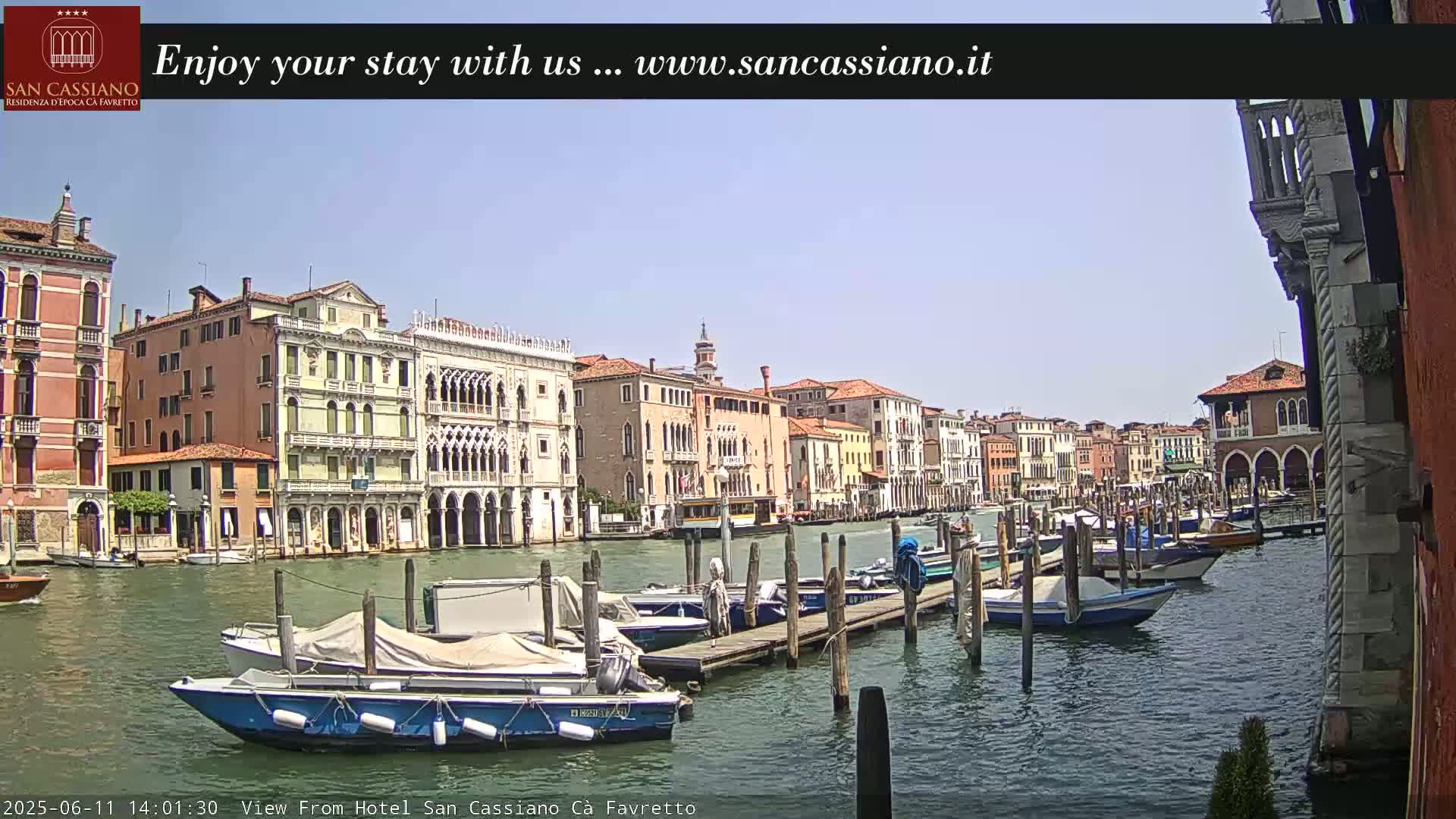 A sunny day in Venice shows a canal lined with historic buildings and numerous boats docked at a pier.