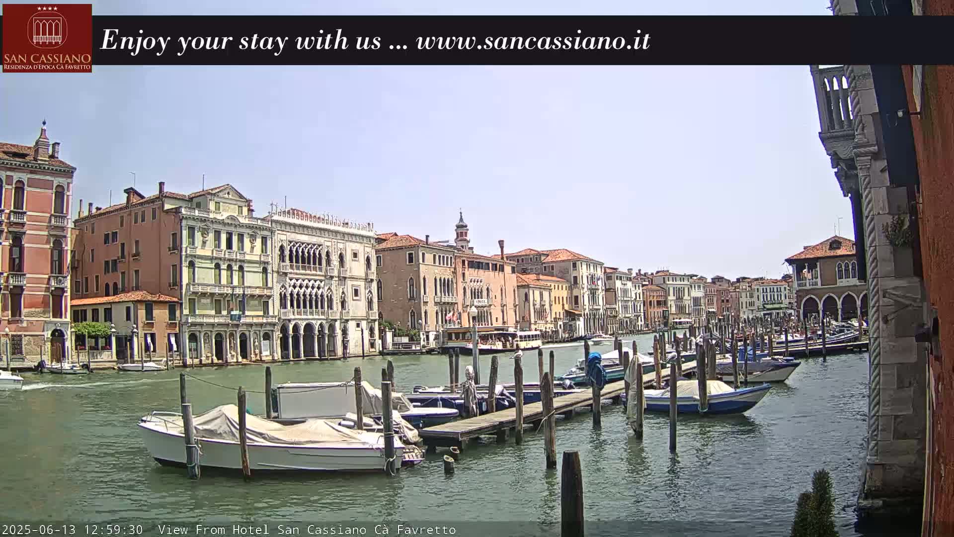 A sunny day in Venice shows a canal lined with historic buildings and several moored boats.