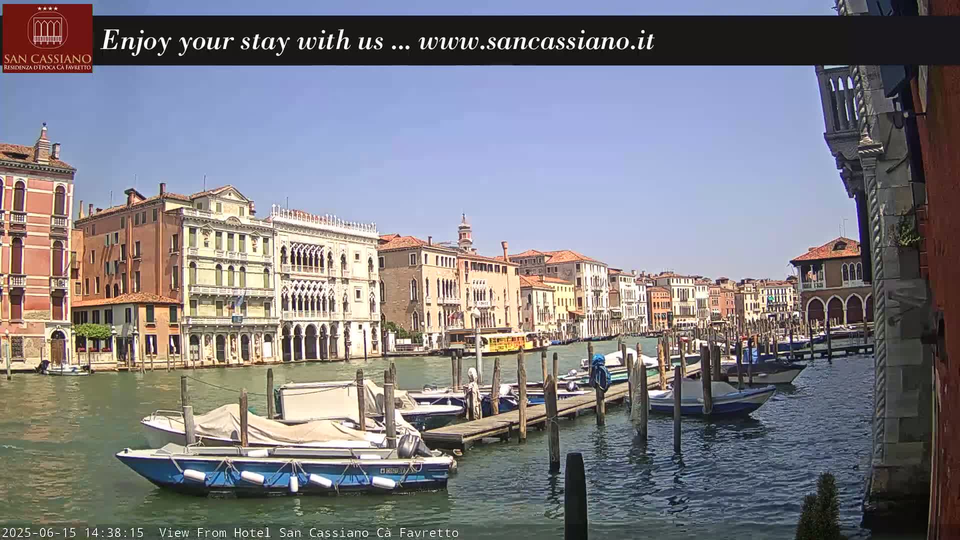 A sunny day in Venice shows a canal lined with colorful buildings and several boats moored at a wooden dock.