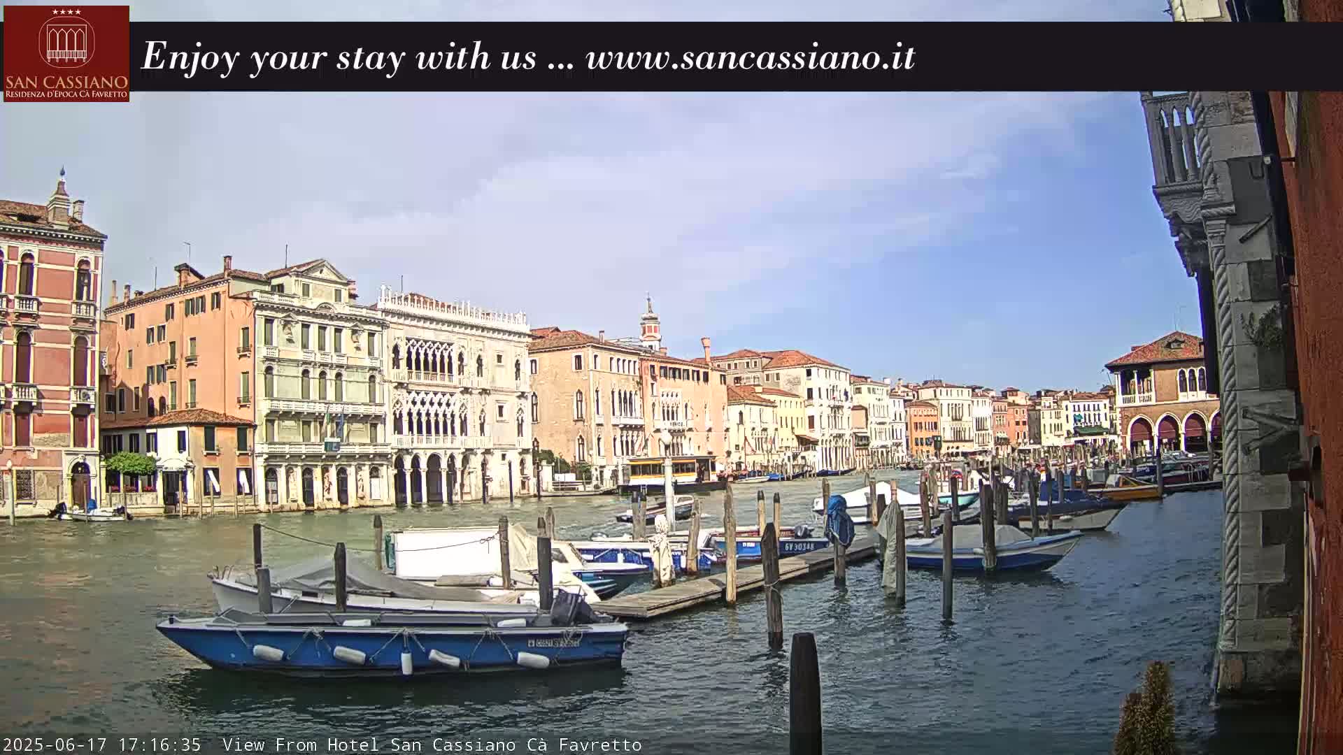 A sunny day in Venice shows a canal lined with colorful buildings and numerous boats moored along the waterway.