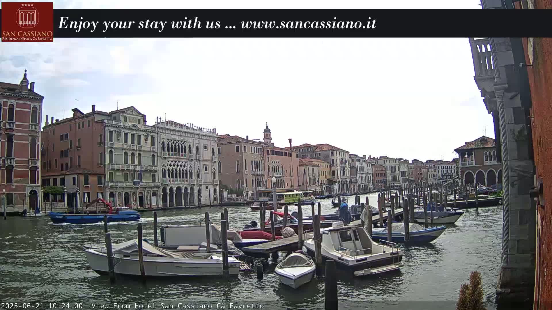 A canal in Venice, Italy, shows several moored boats under a partly cloudy sky.
