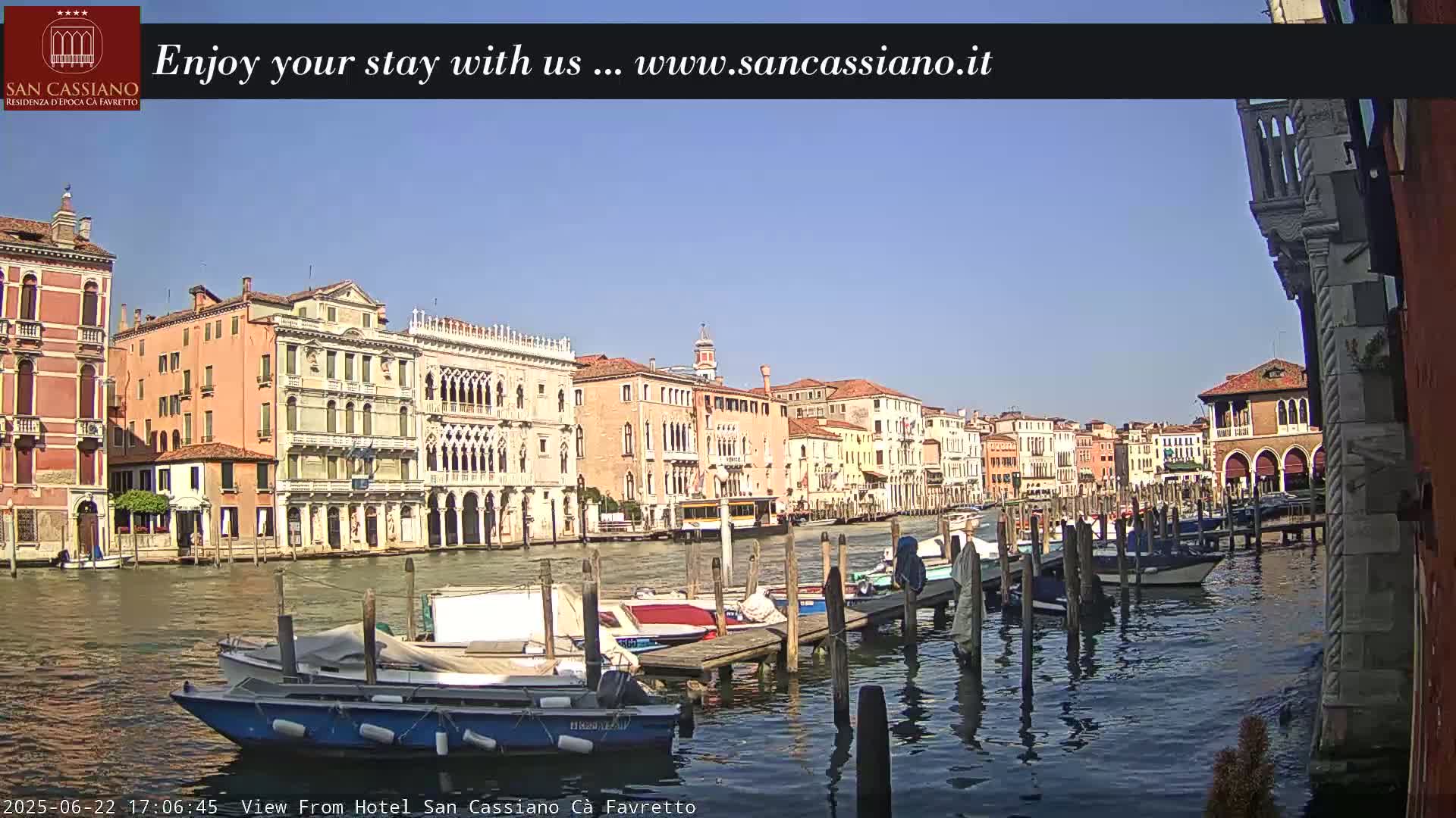 Several colorful buildings line a canal, where many boats are moored to wooden docks under a clear blue sky.