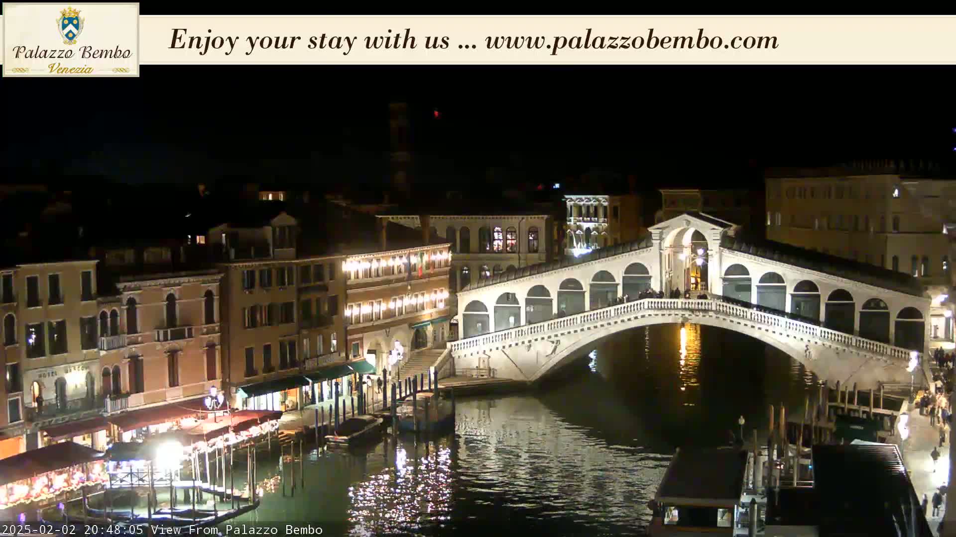 A nighttime view of a bridge over a canal in Venice, with illuminated buildings lining the waterway.