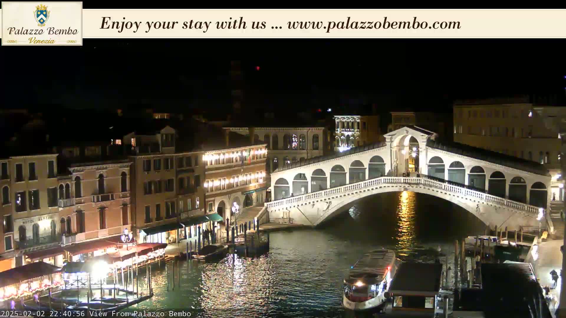 A nighttime view of a canal in Venice, showing a lit-up bridge and buildings along the waterway.