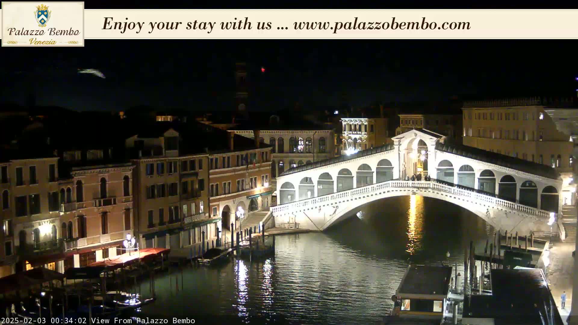 A nighttime view of a canal in Venice, showing a bridge illuminated against a dark sky.