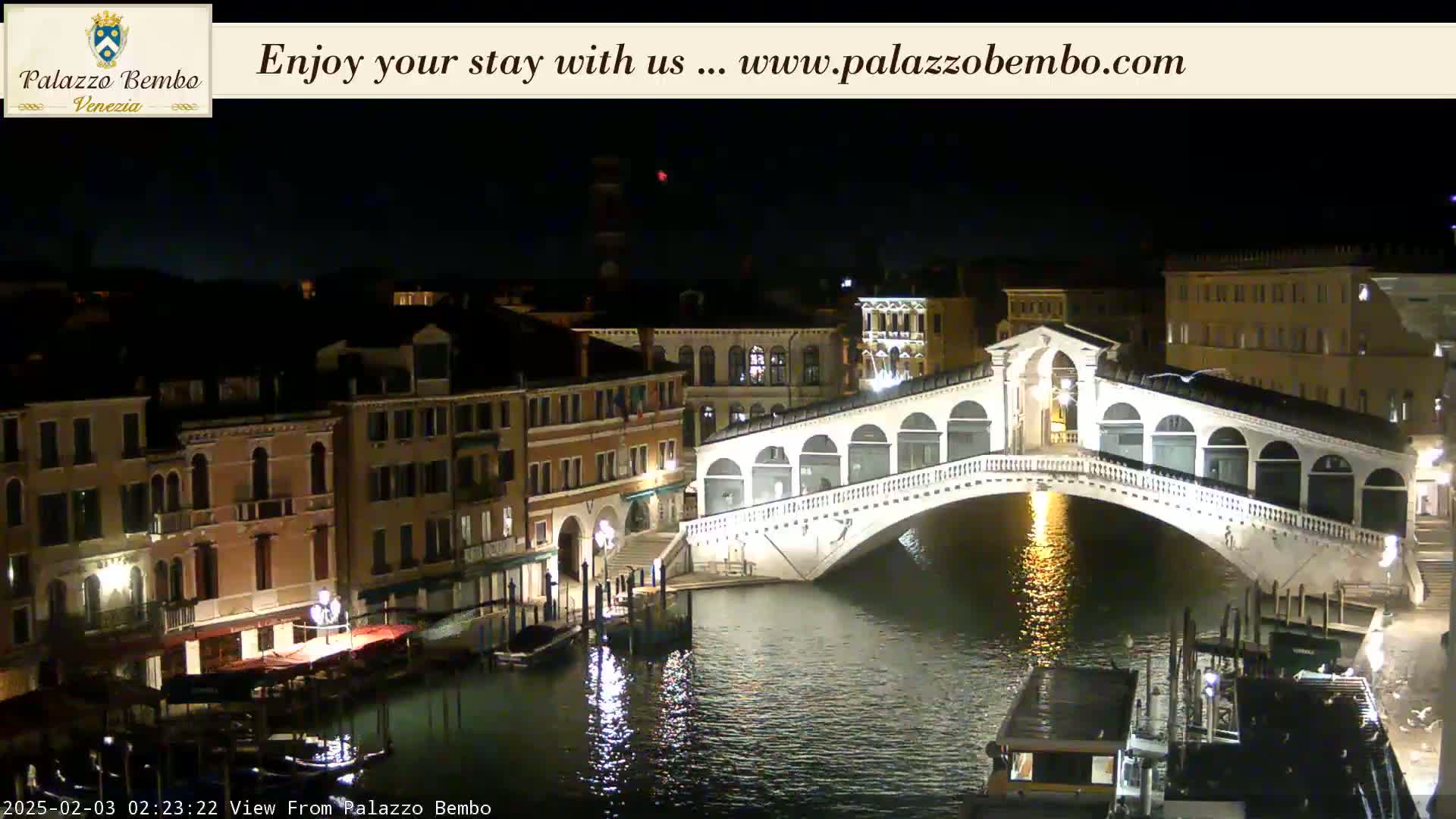 A nighttime view of a canal in Venice, with a lit-up bridge and buildings along the waterway, under a clear, dark sky.