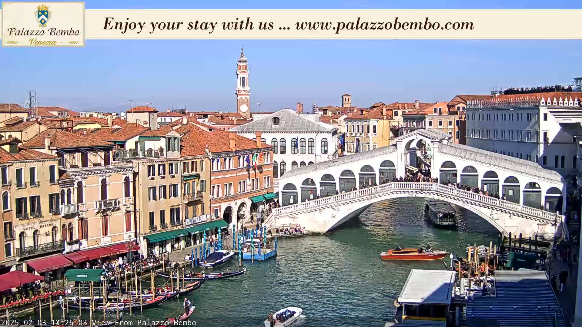 A sunny day in Venice shows a canal with gondolas and a bridge crowded with people.