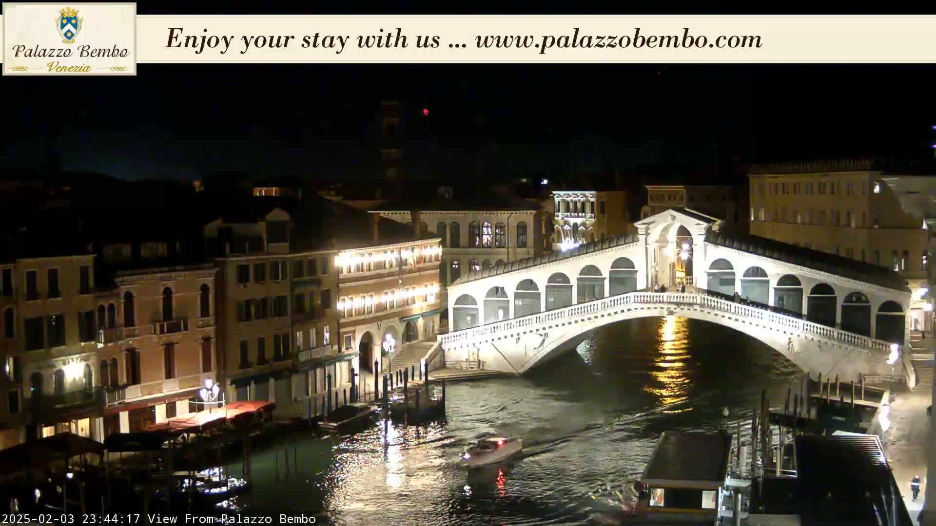 A nighttime view of a canal in Venice, showing a bridge illuminated against a dark sky.