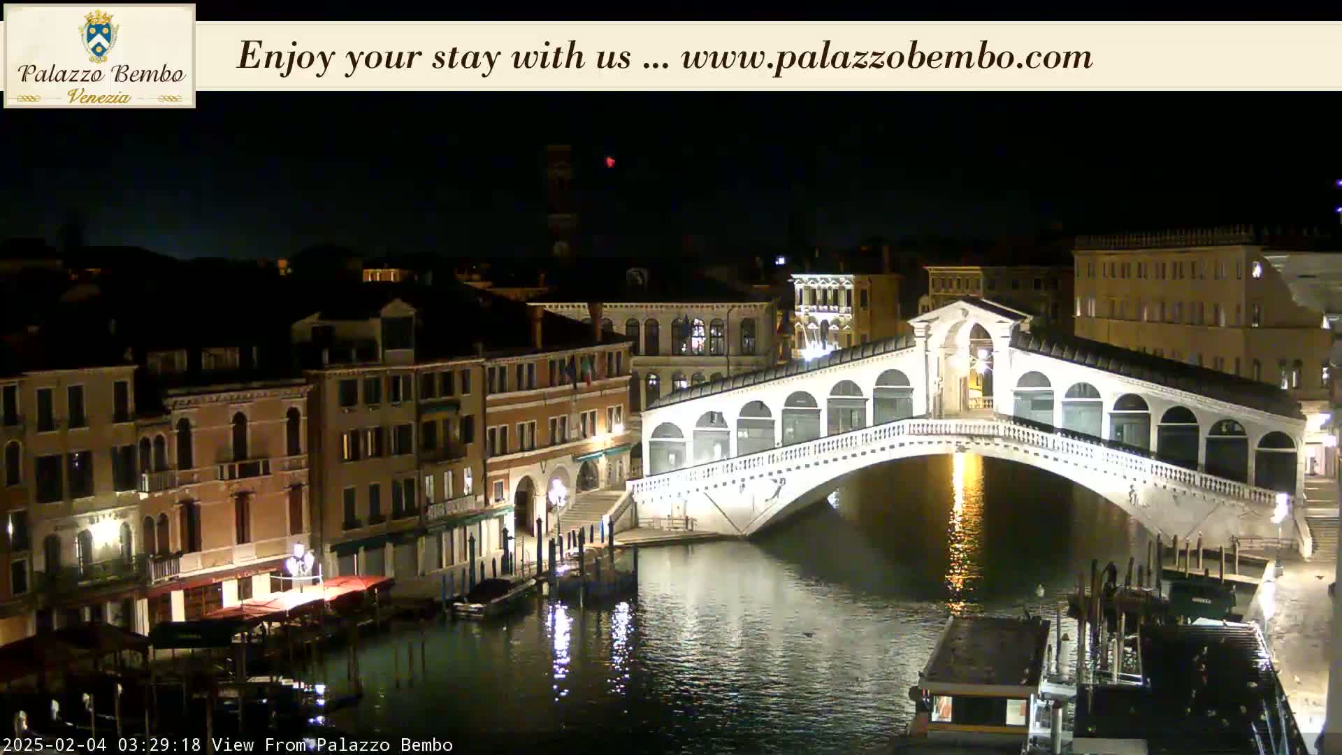 A nighttime view of a canal in Venice, showing a bridge illuminated against a dark sky.
