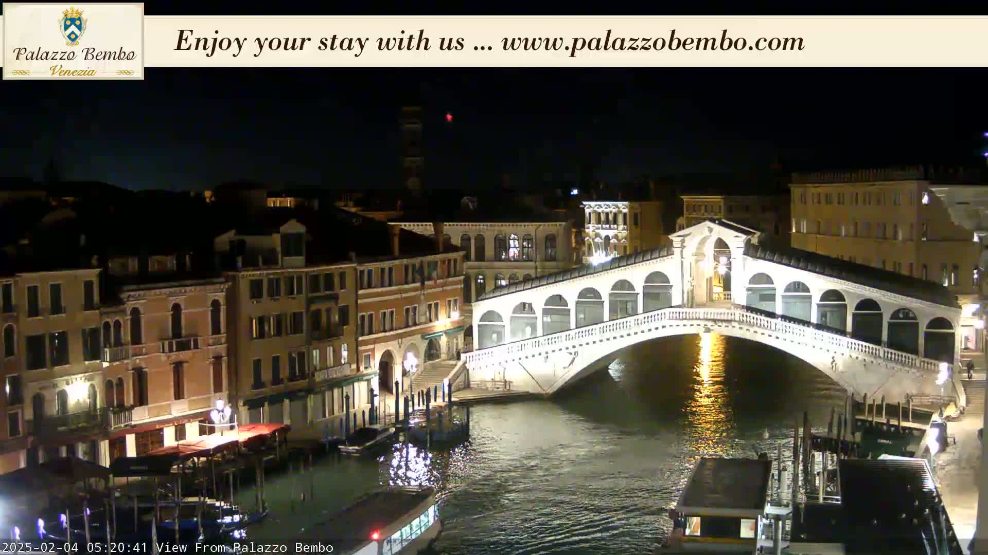 A nighttime view of a bridge over a canal in Venice, with illuminated buildings lining the waterway.