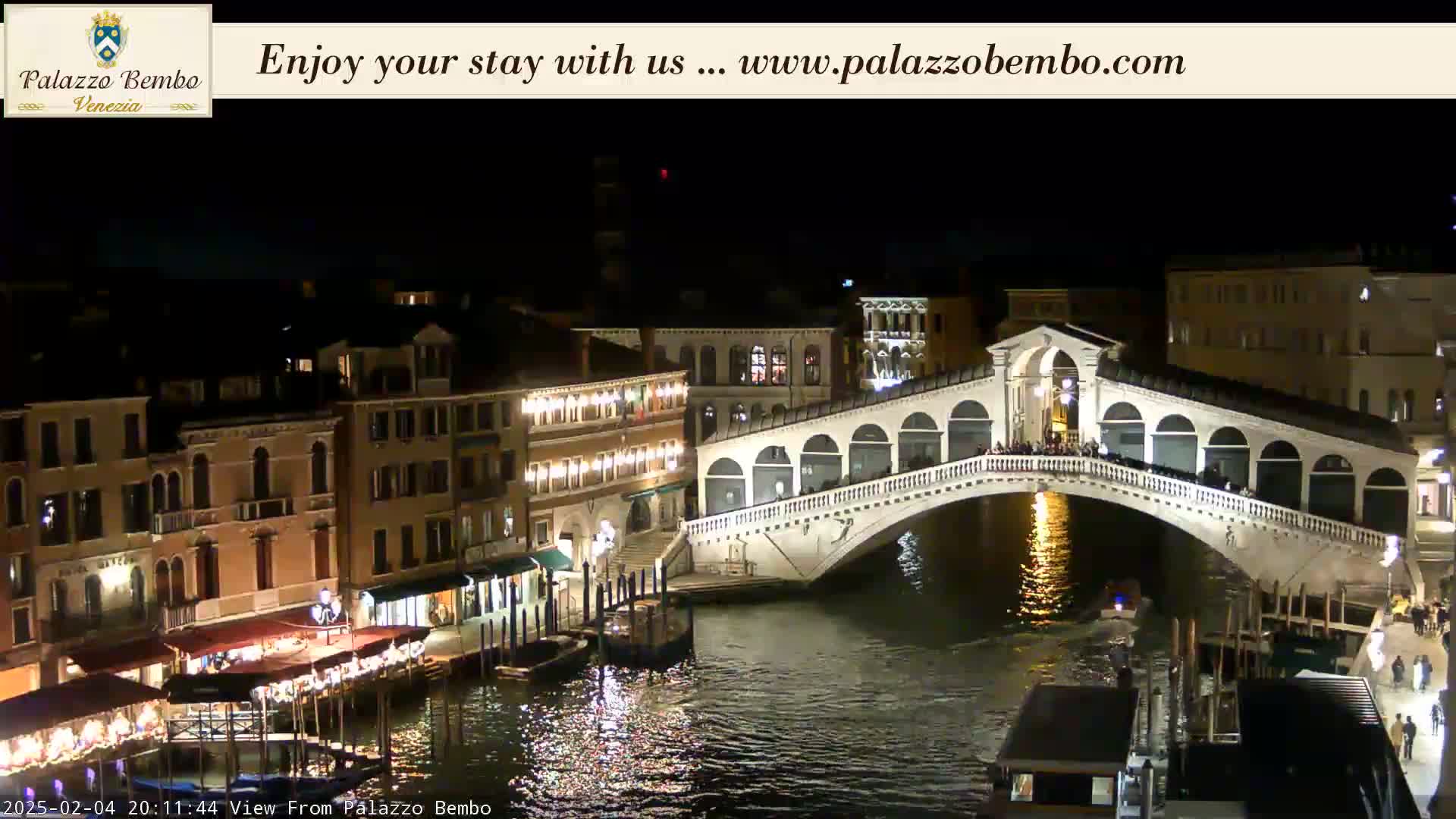 A nighttime view of a bridge over a canal in Venice, with buildings lit along the water's edge.
