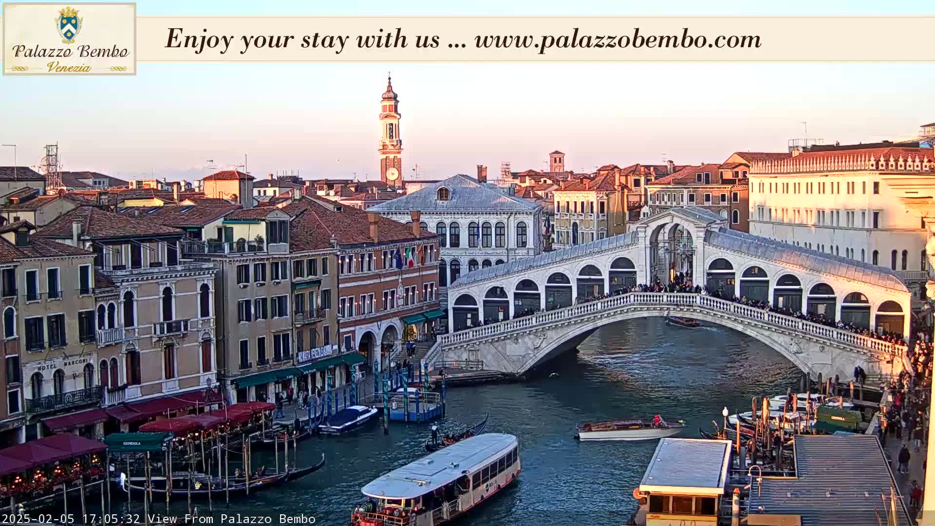 A Venetian canal scene at sunset shows a bridge crowded with people, boats on the water, and buildings lining the waterway.