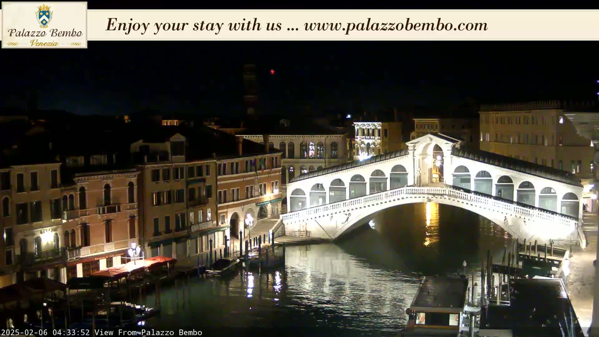 A nighttime view of a canal in Venice, with a bridge illuminated, and buildings lining the waterway.