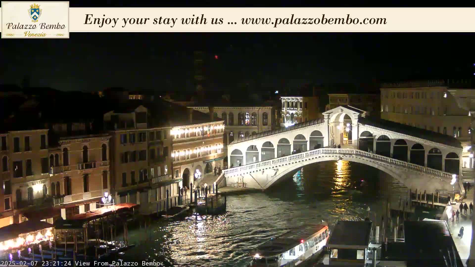 A nighttime view of a bridge over a canal in Venice, with illuminated buildings lining the waterway.