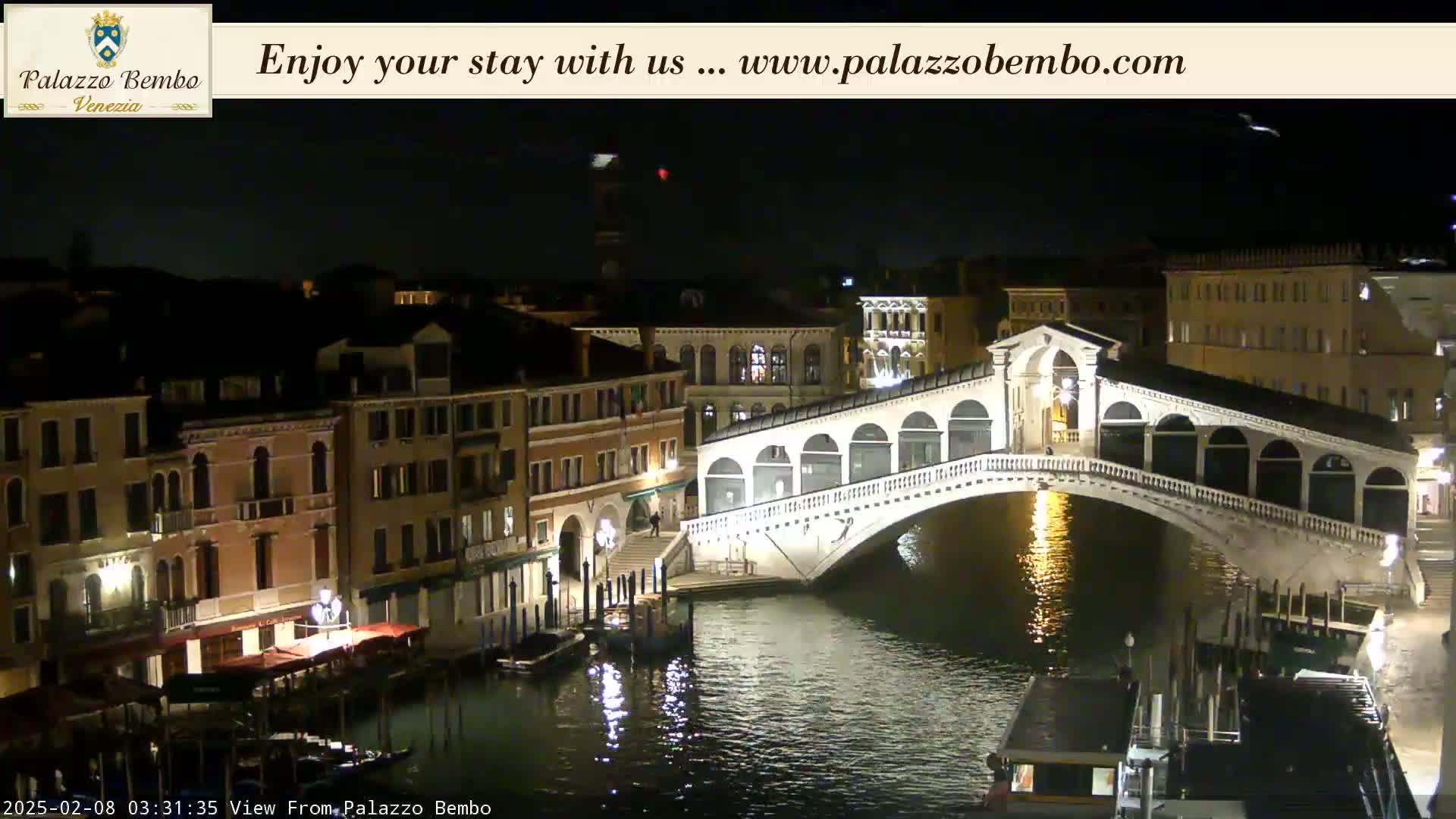 A nighttime view of a bridge spanning a canal in Venice, with buildings lining the waterway under a clear, dark sky.