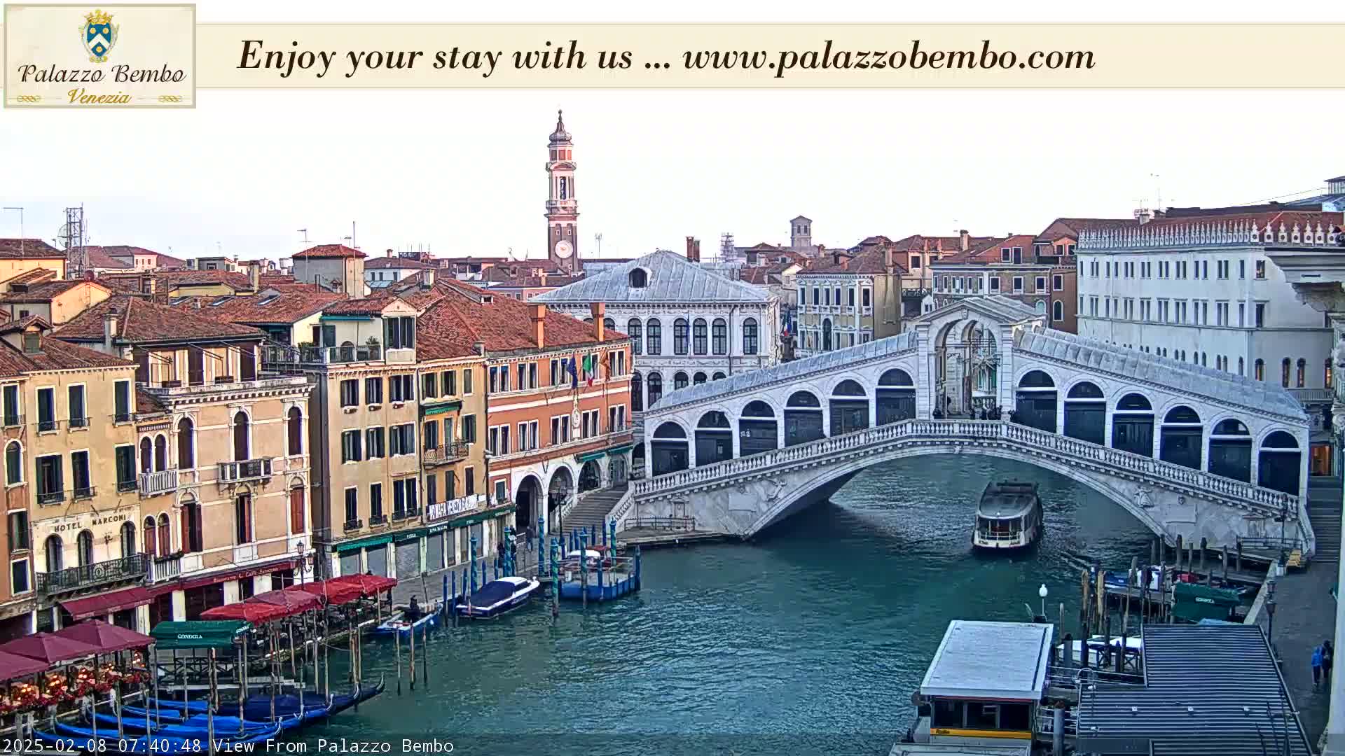 A Venetian canal scene shows a bridge, several buildings, and boats under a mostly cloudy sky.