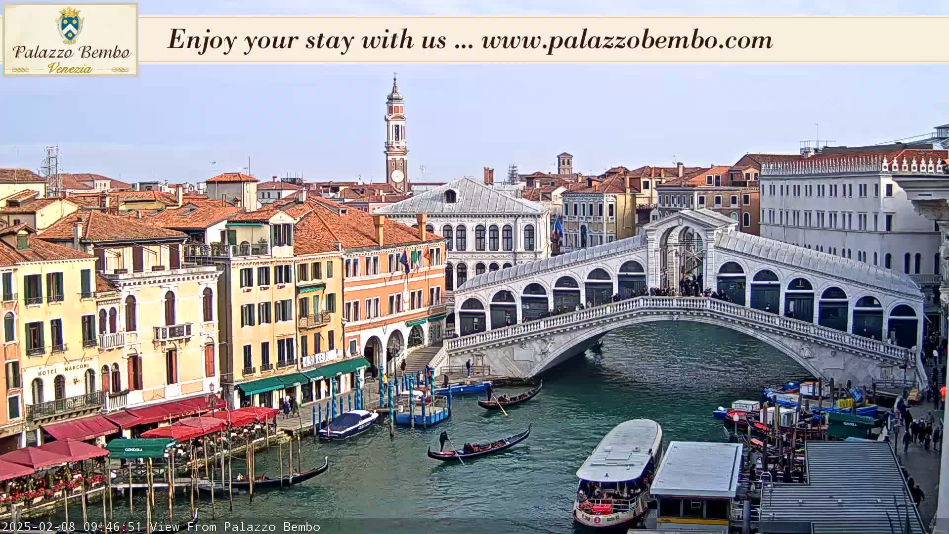 A canal in Venice, under a clear sky, features gondolas, a bridge, and colorful buildings lining the waterway.