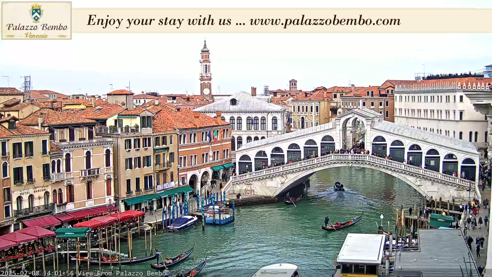 A canal in Venice, under a cloudy sky, shows a bridge crowded with people, gondolas on the water, and buildings lining the waterway.