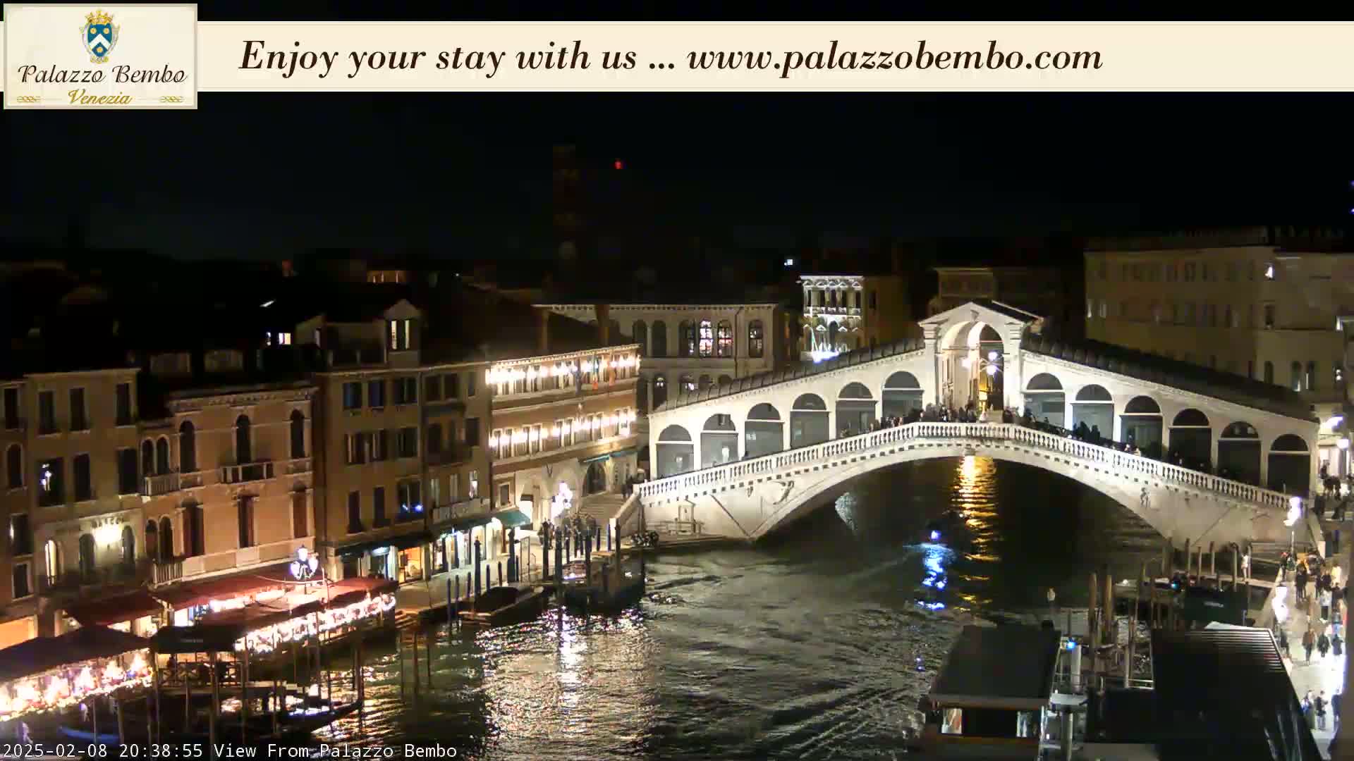 A nighttime view of a bridge over a canal in Venice, with illuminated buildings lining the waterway.