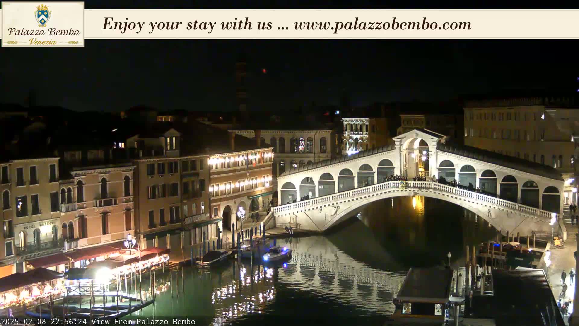 A nighttime view of a canal in Venice, showing a bridge illuminated with lights and buildings along the water's edge.