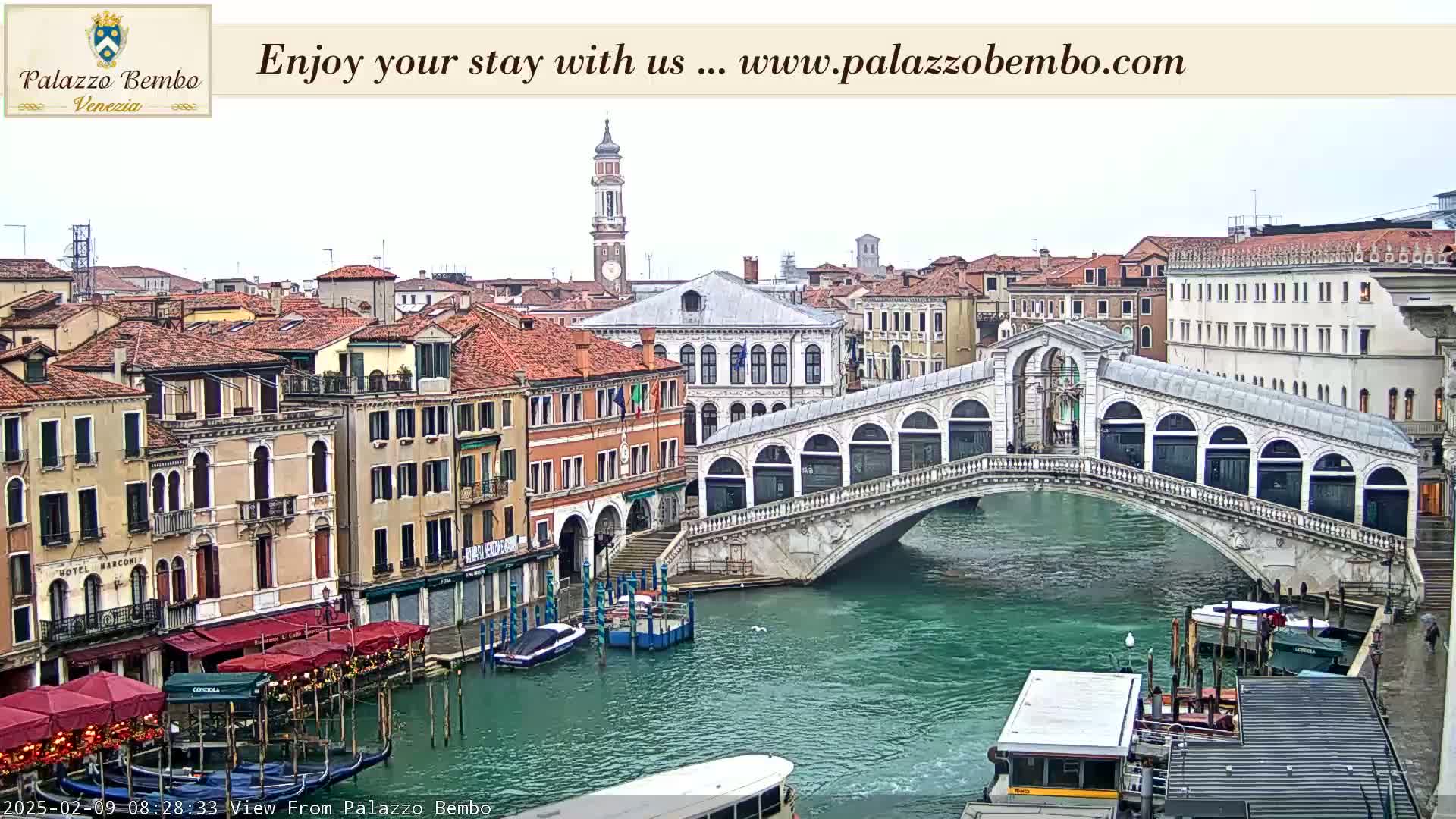 A view of a canal in Venice, showing a bridge with arched walkways and buildings lining the waterway under an overcast sky.